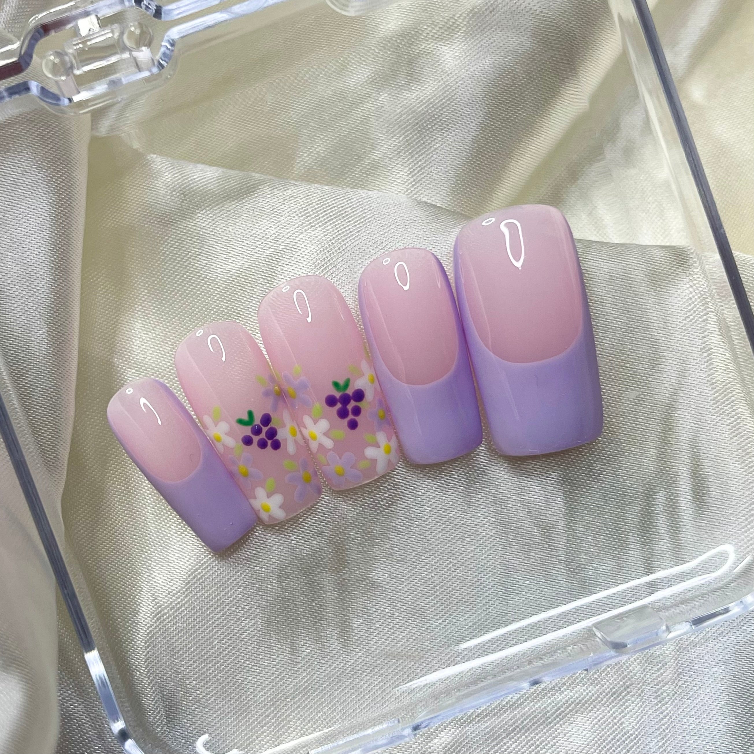 Grape Escape press-on nails with purple French tips, floral designs, hand-painted grapes, and pinky nude bases. Perfect for a fruity, spring-inspired look.