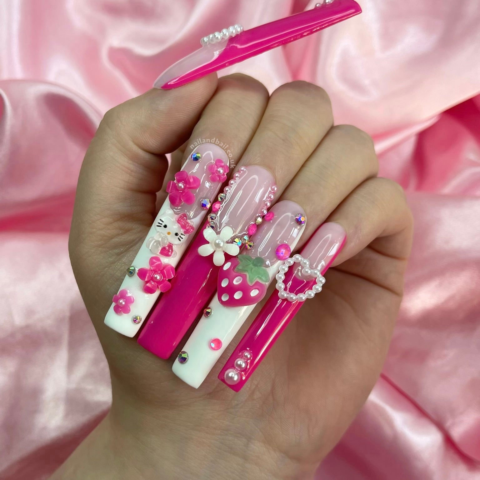 Pink and white French tip press-on nails with kitty charms, pearls, and heart nail art