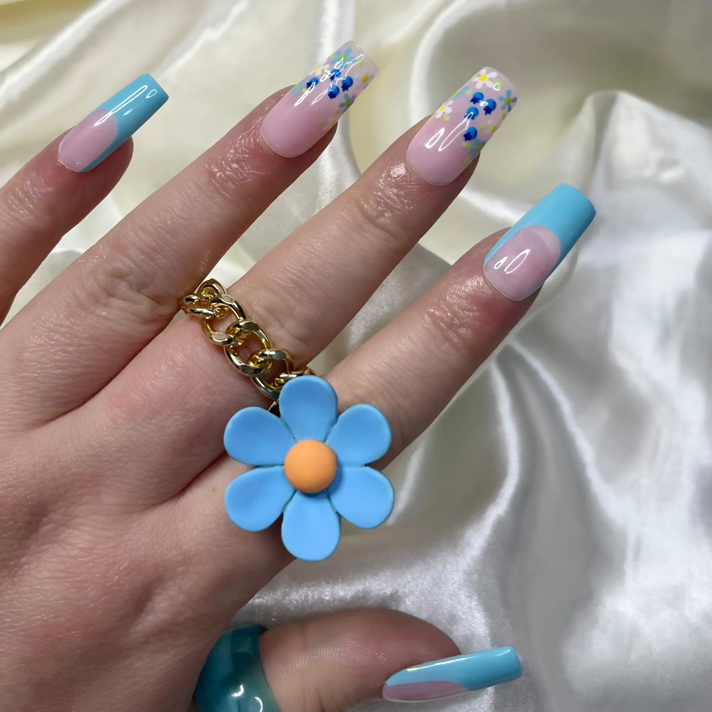 Blueberry Fields press-on nails feature blue French tips, floral designs, hand-painted blueberries, and soft pinky nude bases for a sweet, botanical spring look.