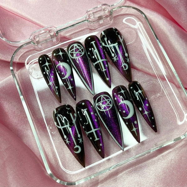 Black and purple cat eye Halloween press-on nails with witch-inspired nail art, moons, stars, and pentacle details