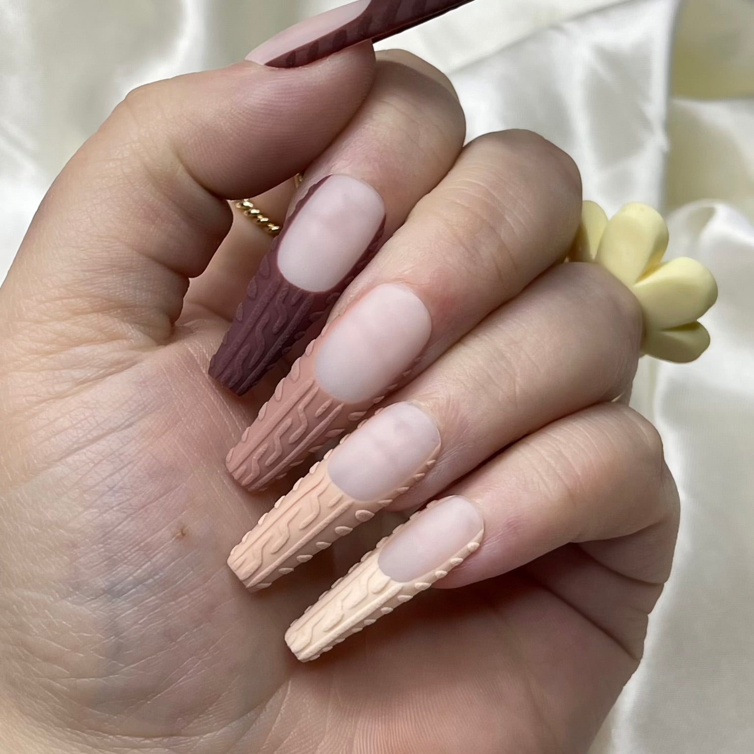 A manicure image showing matte nude French tips with a sweater-knit design on the nails