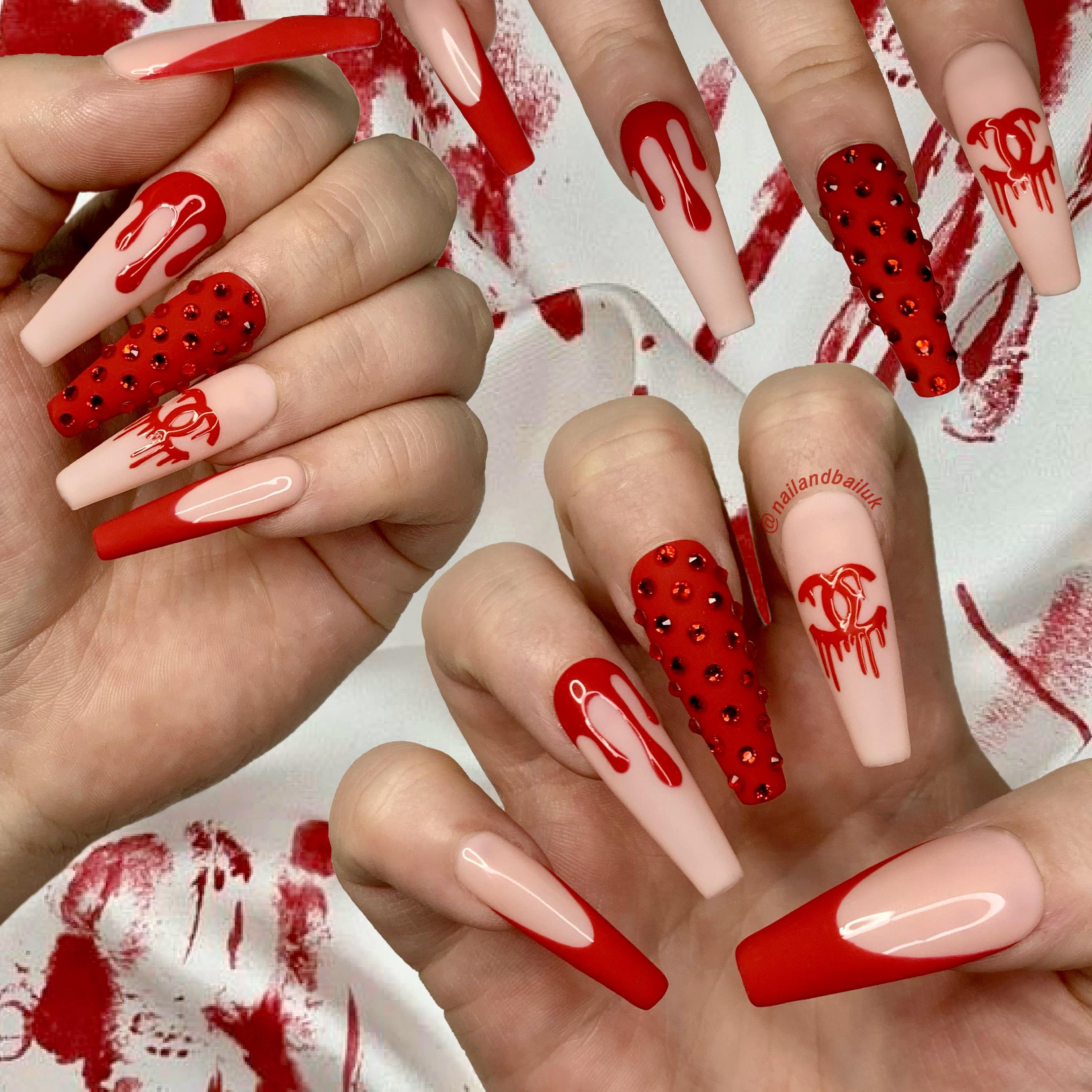 Nude press-on nails with matte red French tips, luxury-inspired drips, and crystal embellishments