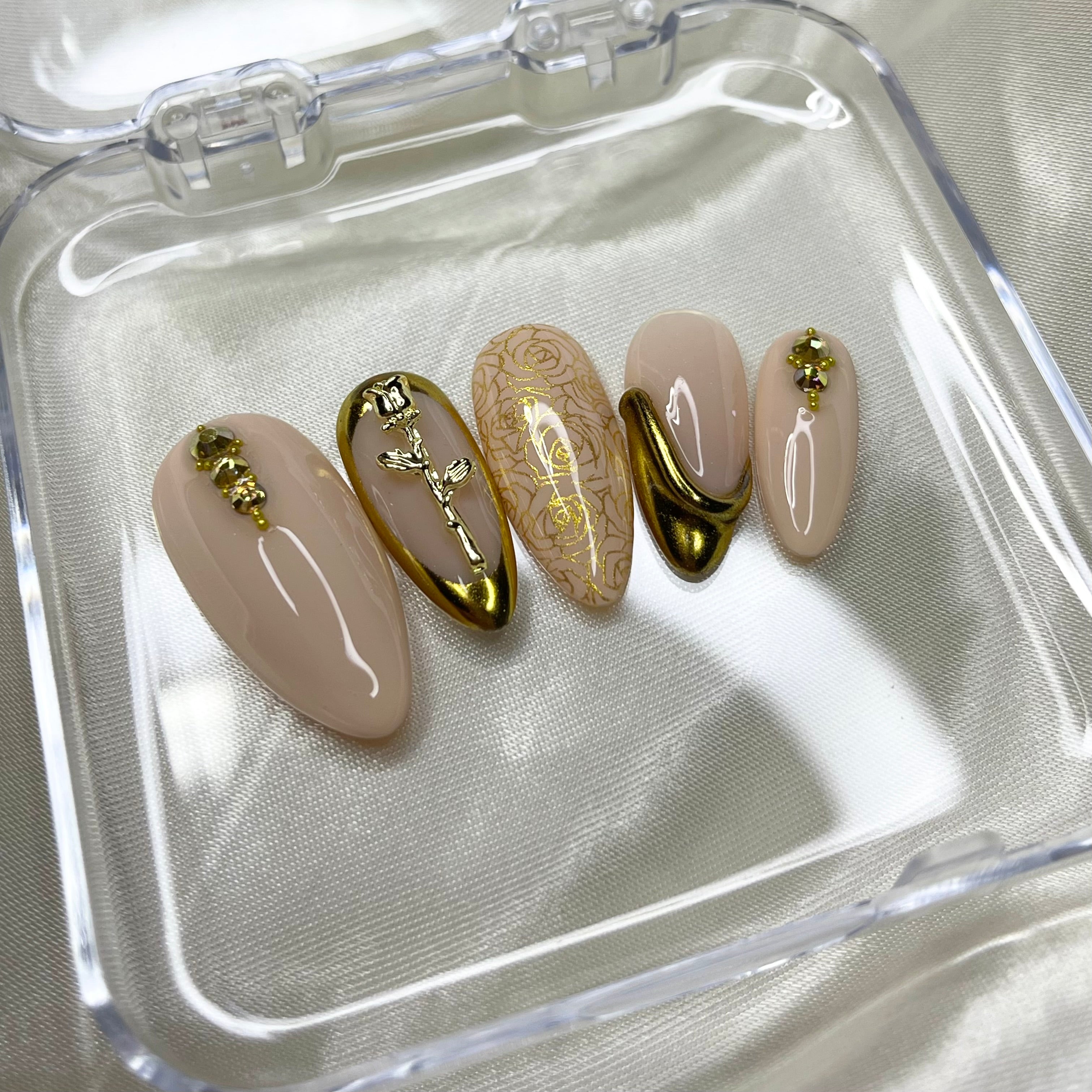 Nude press-on nails with gold rose charms, gold crystal details, and luxury 3D nail art