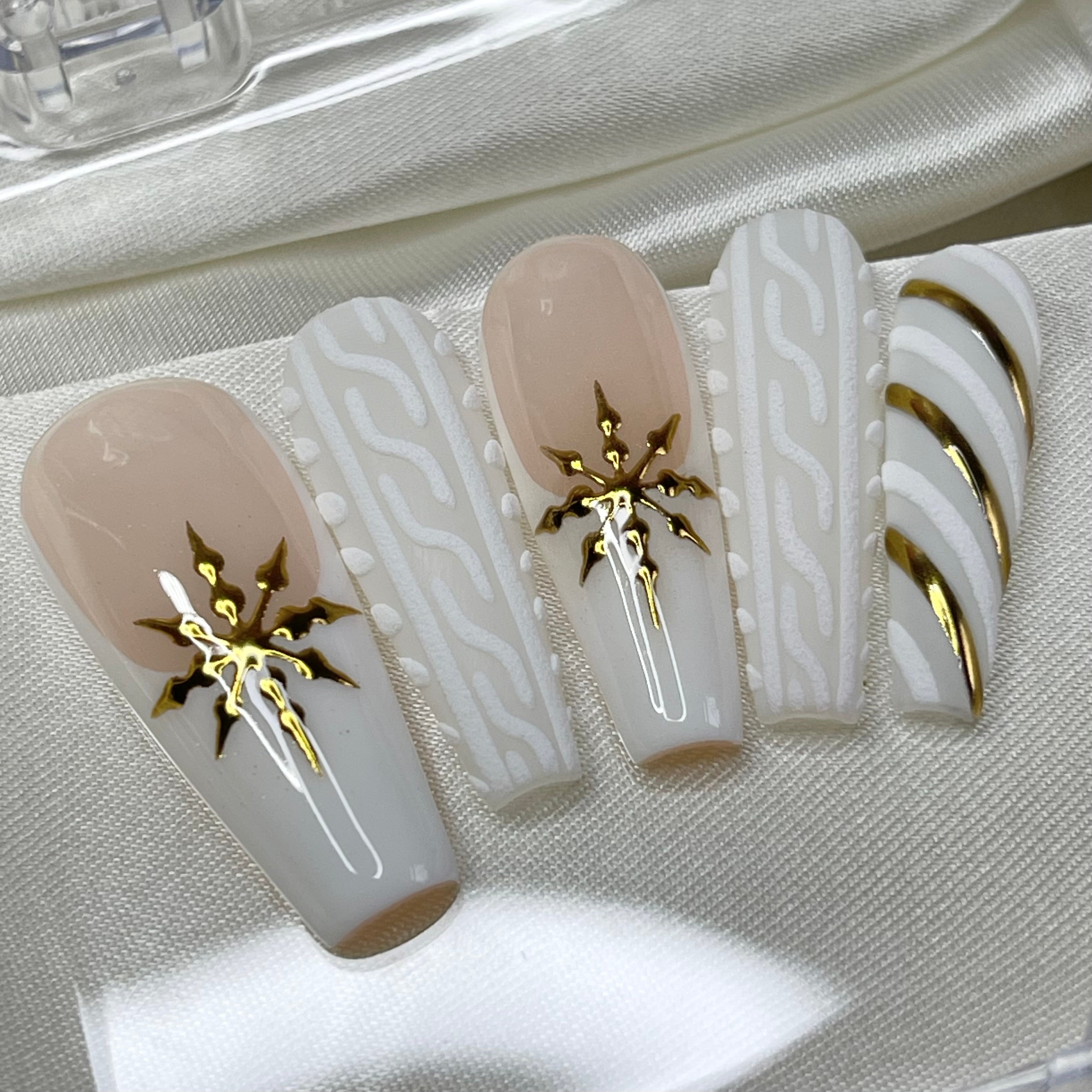 Nude and white Christmas press-on nails with gold snowflakes, sweater nail art, and candy cane details