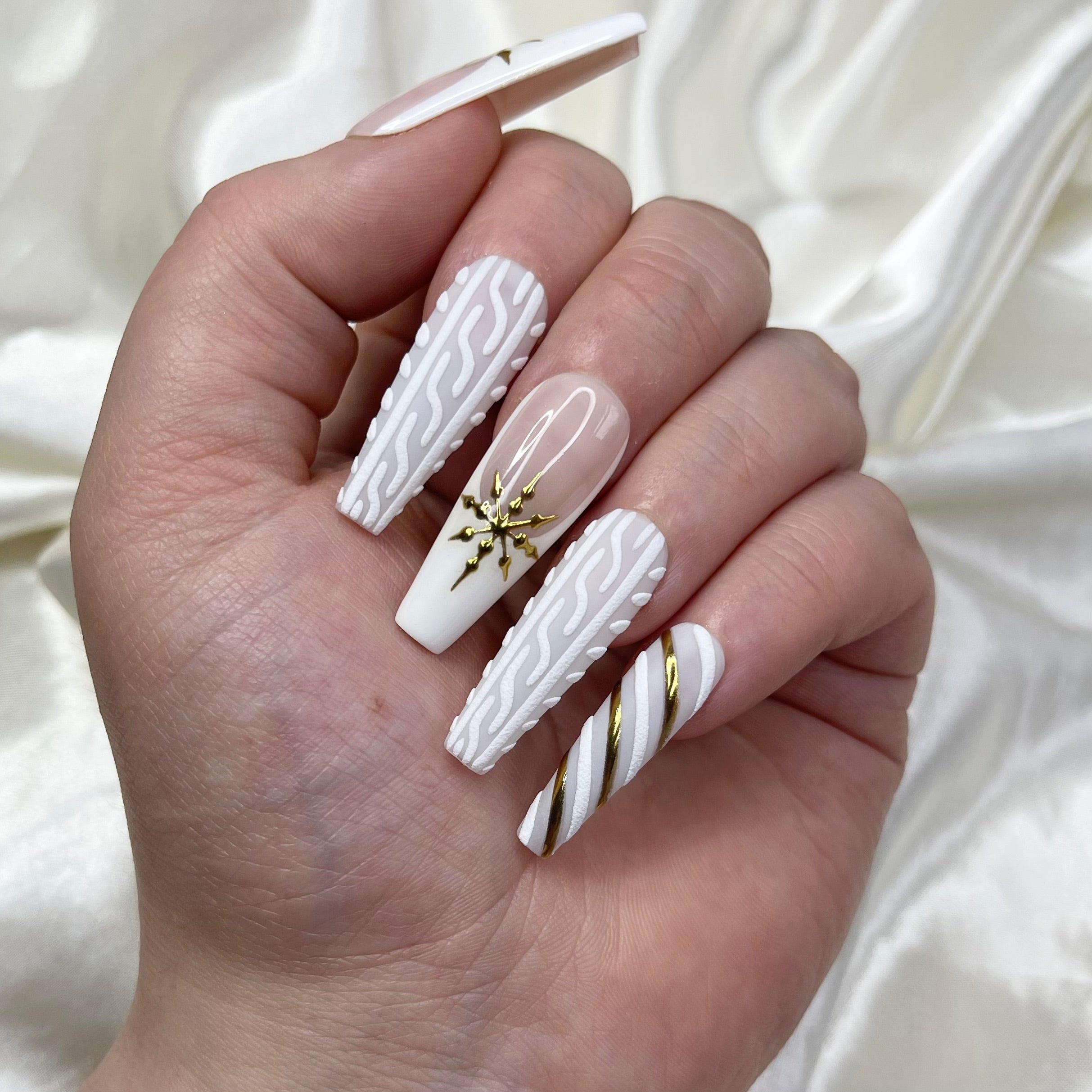 Glossy handmade winter press-on nails featuring nude and white French tips with gold snowflake nail art, embossed sweater texture details, and candy cane stripe designs for a festive holiday manicure.
