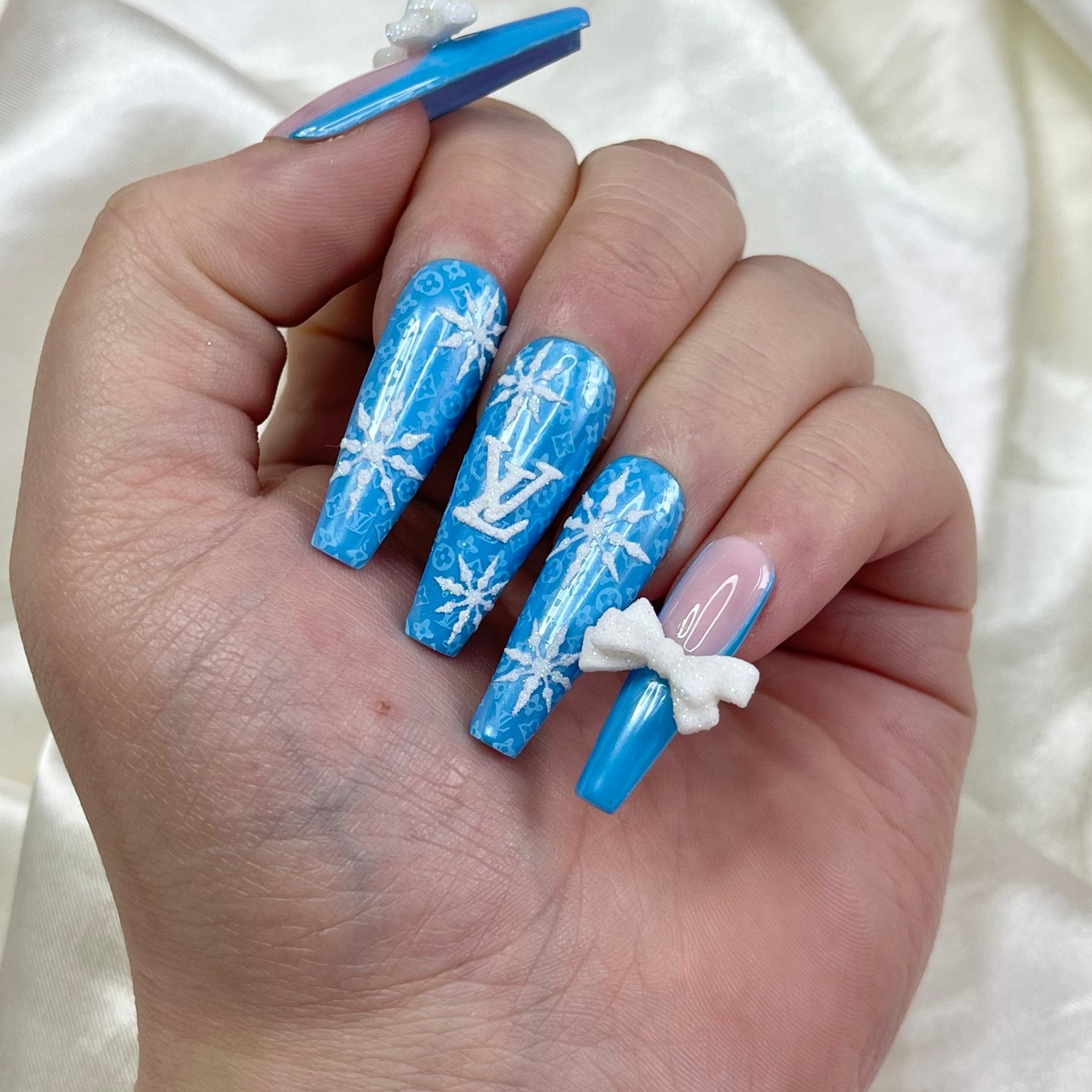 A set of press-on nails featuring a combination of pink and blue colors with white snowflake patterns and glittered logos.