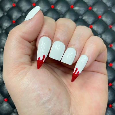 White vampire-inspired press-on nails with red shimmer fang nail art