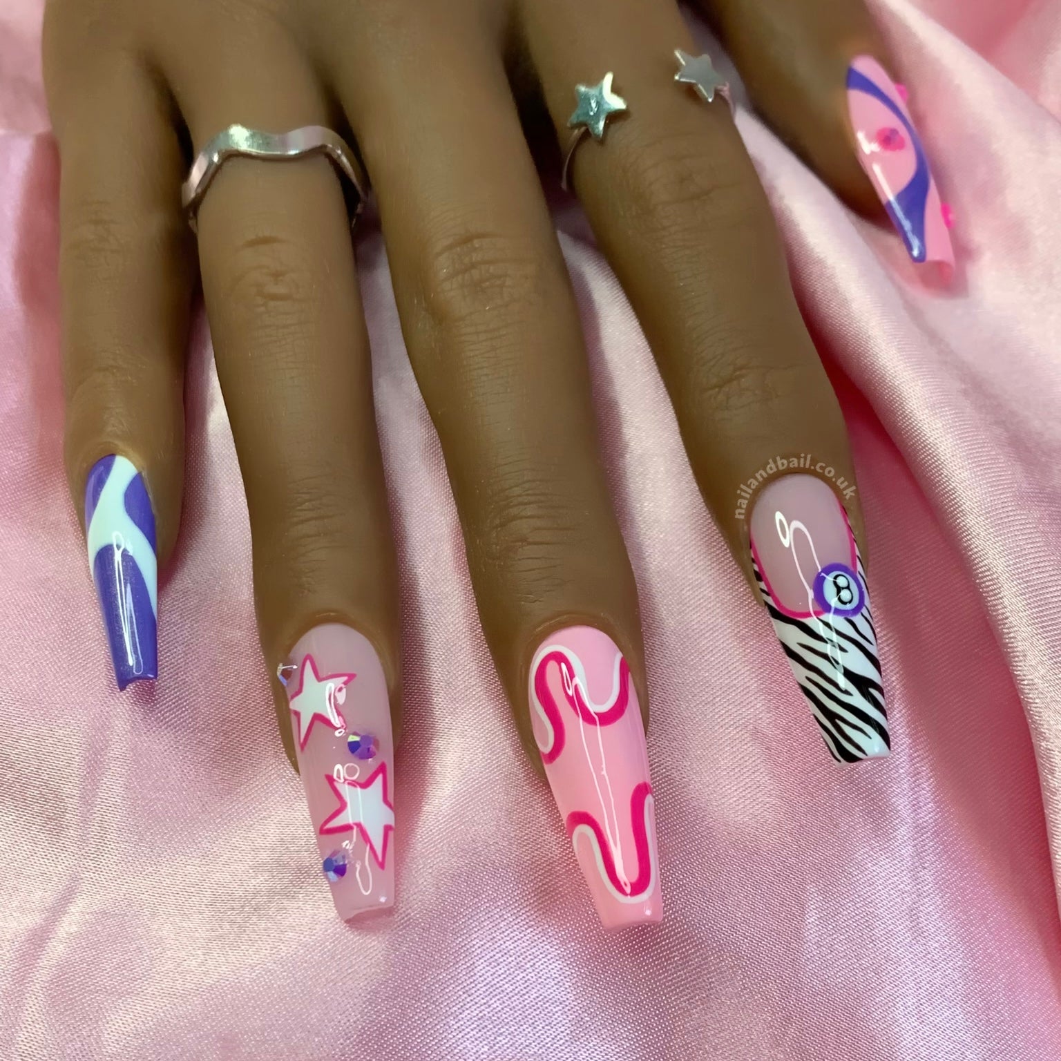A set of press-on nails featuring a variety of designs including pink and purple stripes, zebra prints, stars, and crystals.