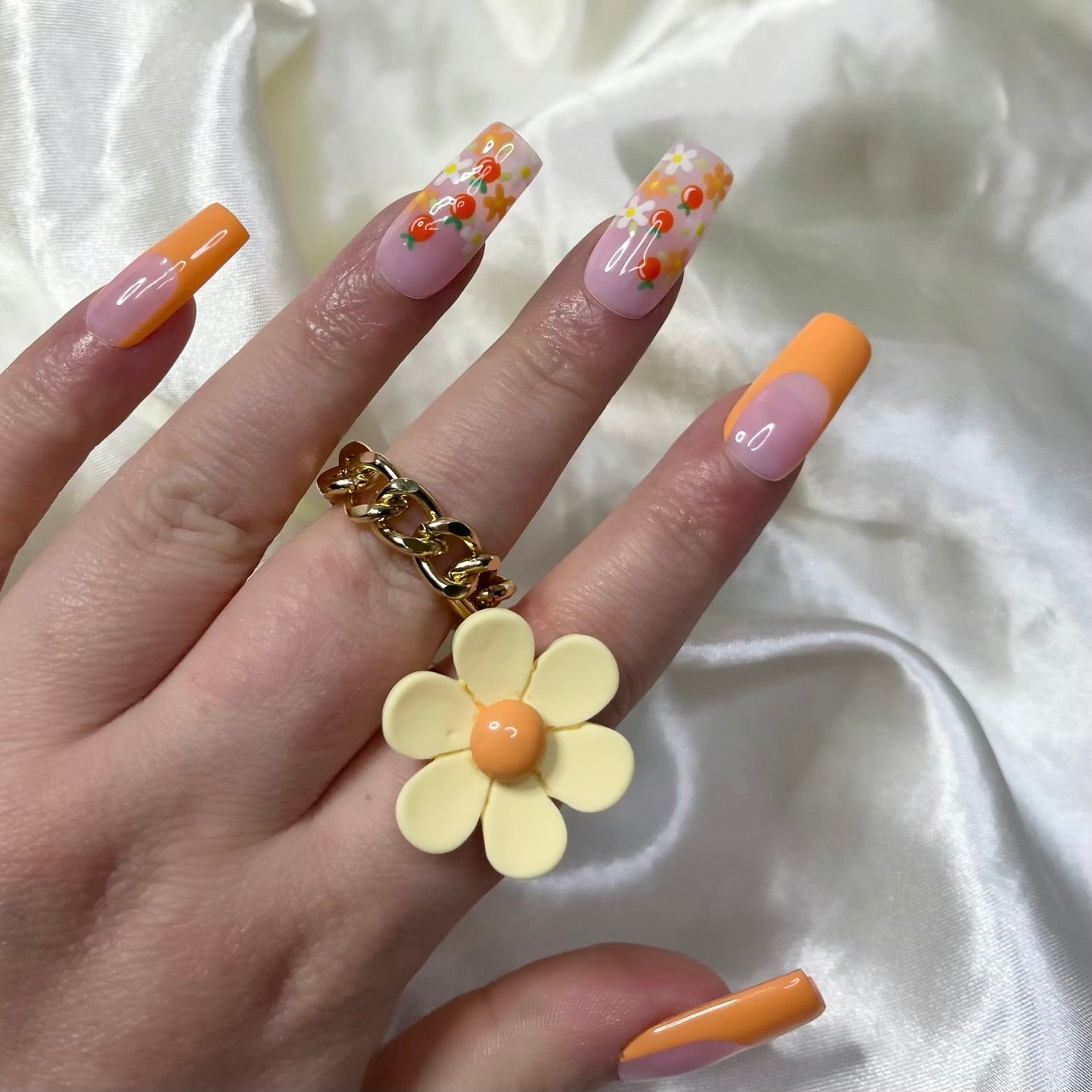 Tangerine Trails press-on nails feature bold orange French tips, white and orange flowers, golden centres, hand-painted oranges, and soft pinky nude bases for a zesty spring look.