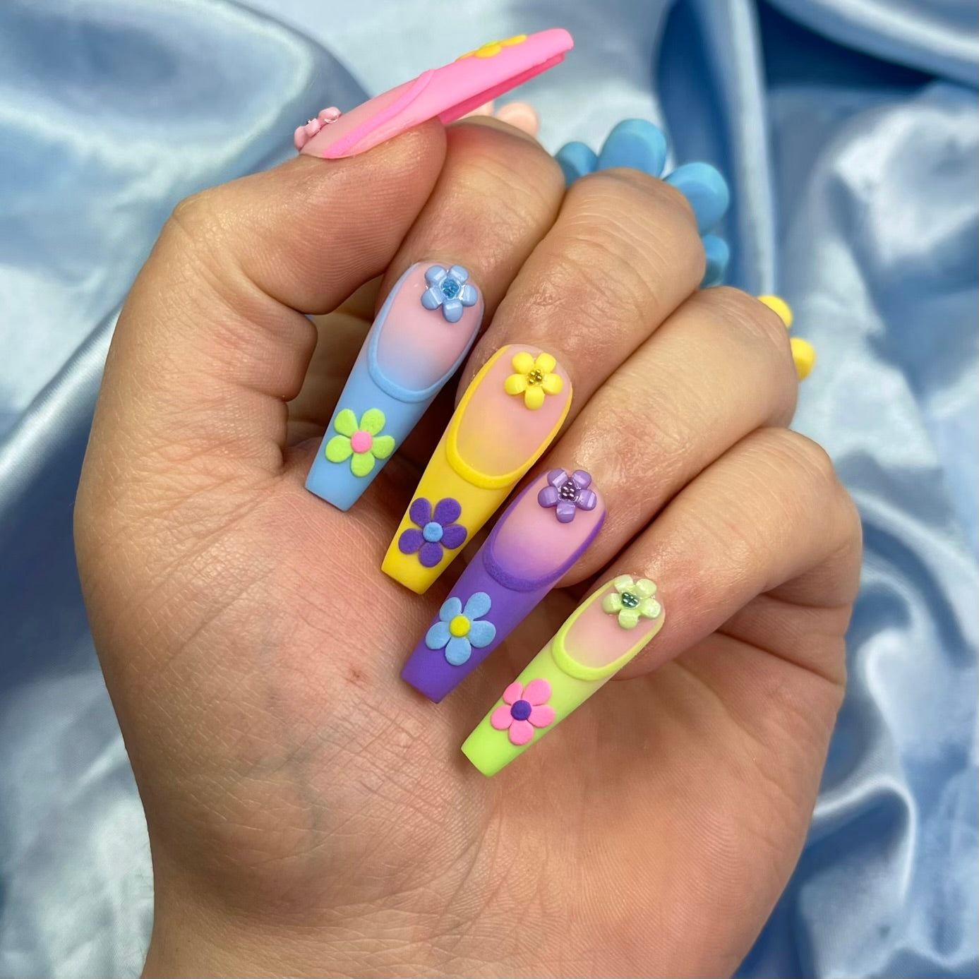 Spring Dream press-on nails feature a pastel ombre design in pink, blue, yellow, purple, and green with embossed French tips and 3D floral details for a chic spring look.