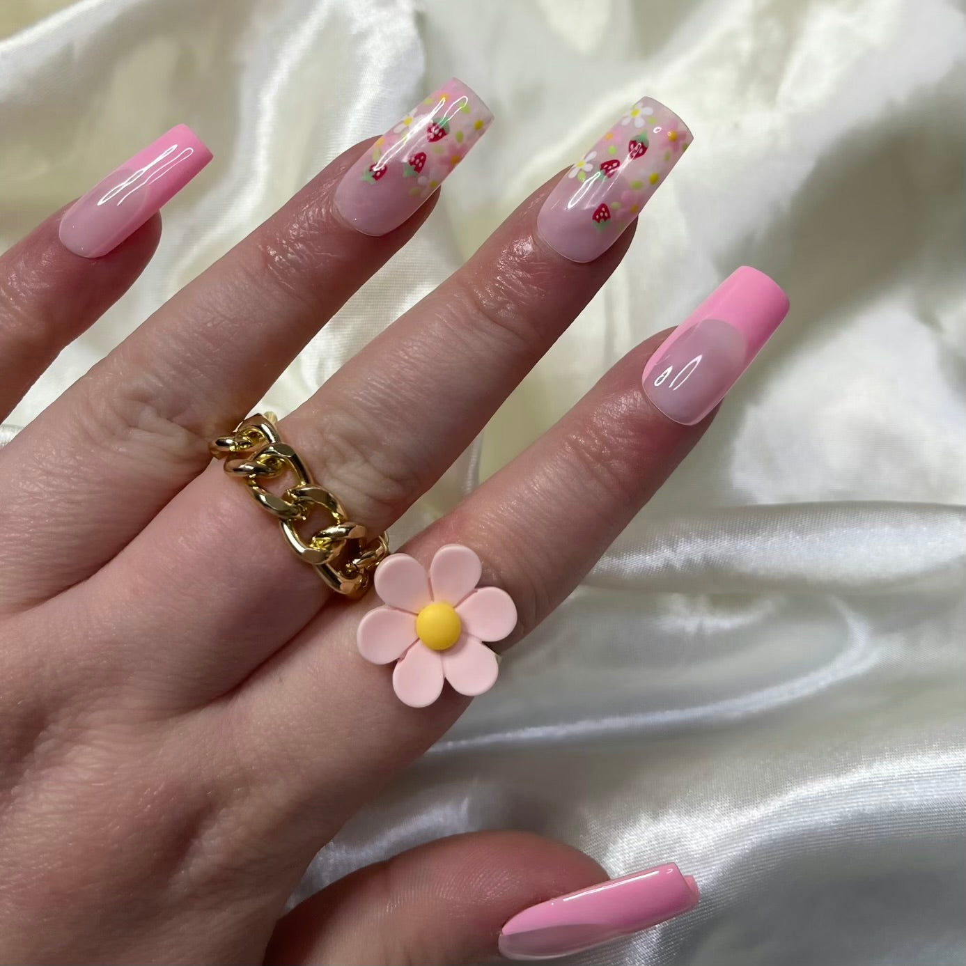 Strawberry Patch press-on nails feature rosy pink French tips, white and pink flowers, golden centres, hand-painted strawberries, and soft pinky nude bases for a fresh, fruity spring look.