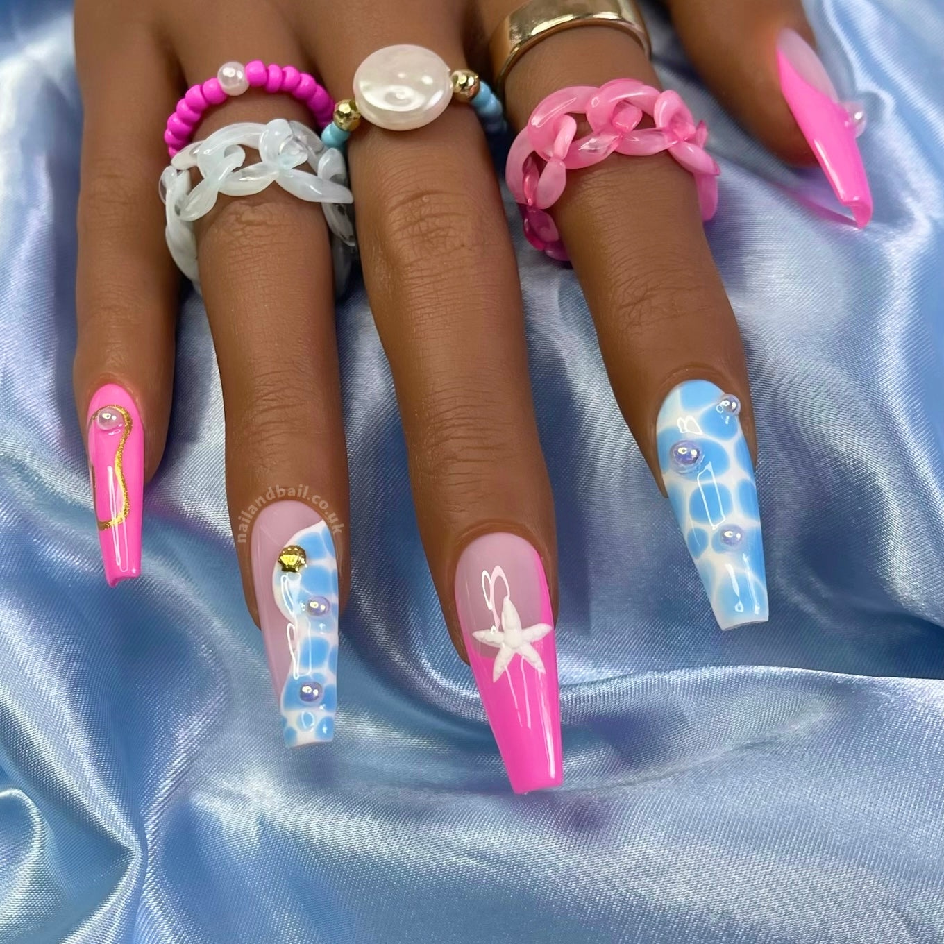 Summer press-on nails with pool-inspired nail art, starfish charms, pearls, and gold shell details