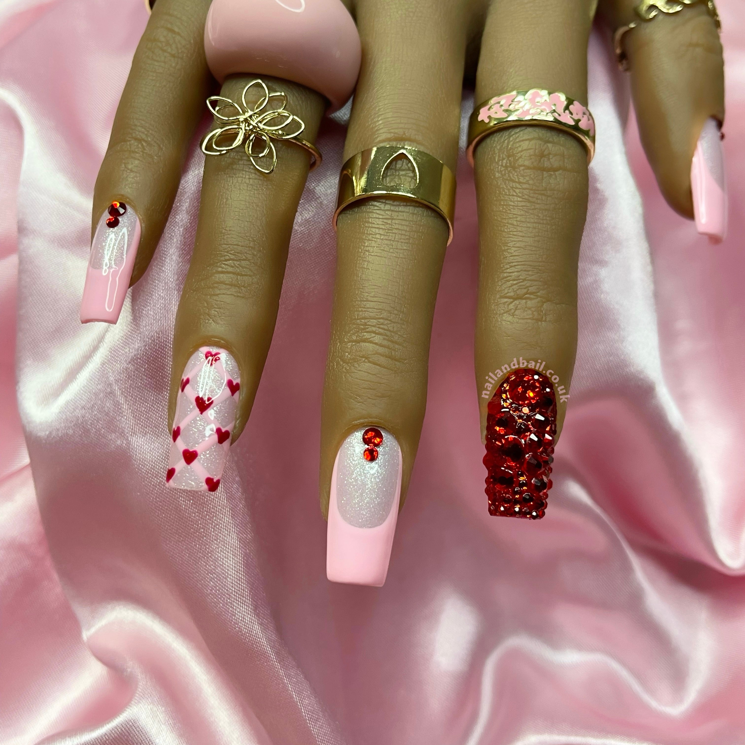 Pink shimmer press-on nails with baby pink French tips, heart nail art, and red crystal details