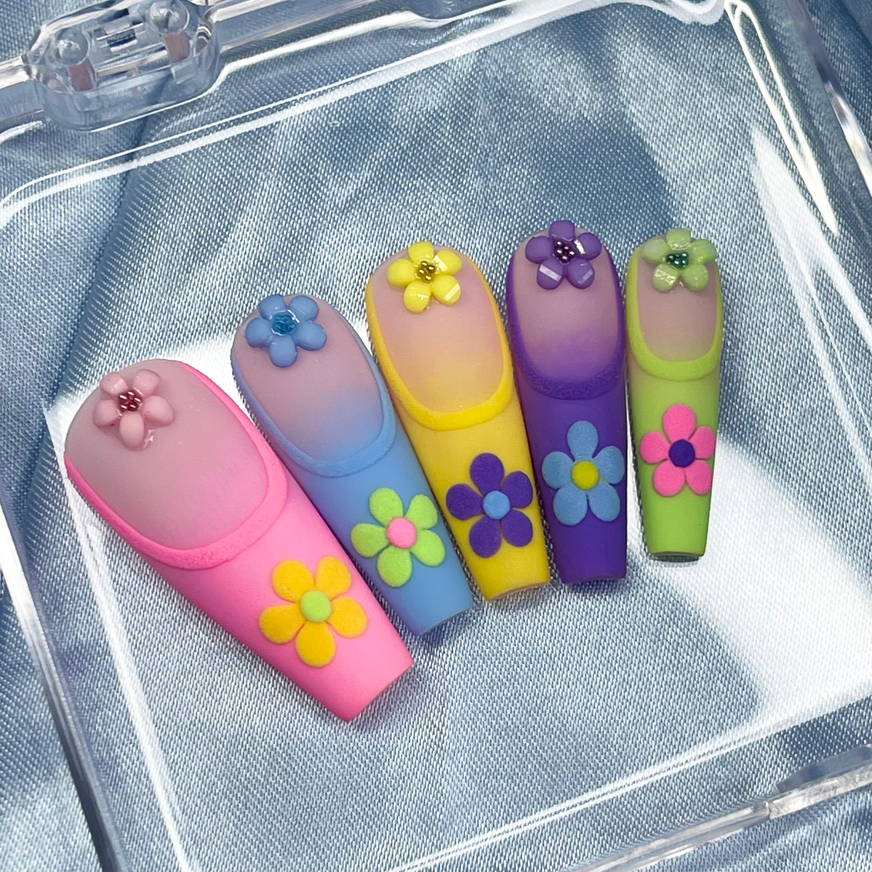 Spring Dream press-on nails feature a pastel ombre design in pink, blue, yellow, purple, and green with embossed French tips and 3D floral details for a chic spring look.