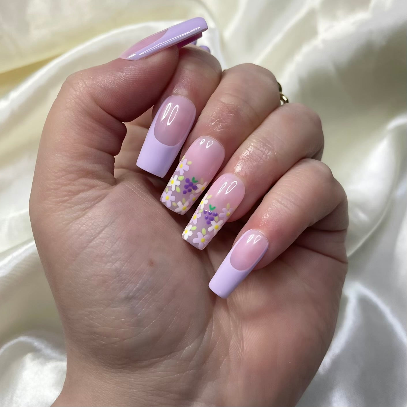 Grape Escape press-on nails with purple French tips, floral designs, hand-painted grapes, and pinky nude bases. Perfect for a fruity, spring-inspired look.