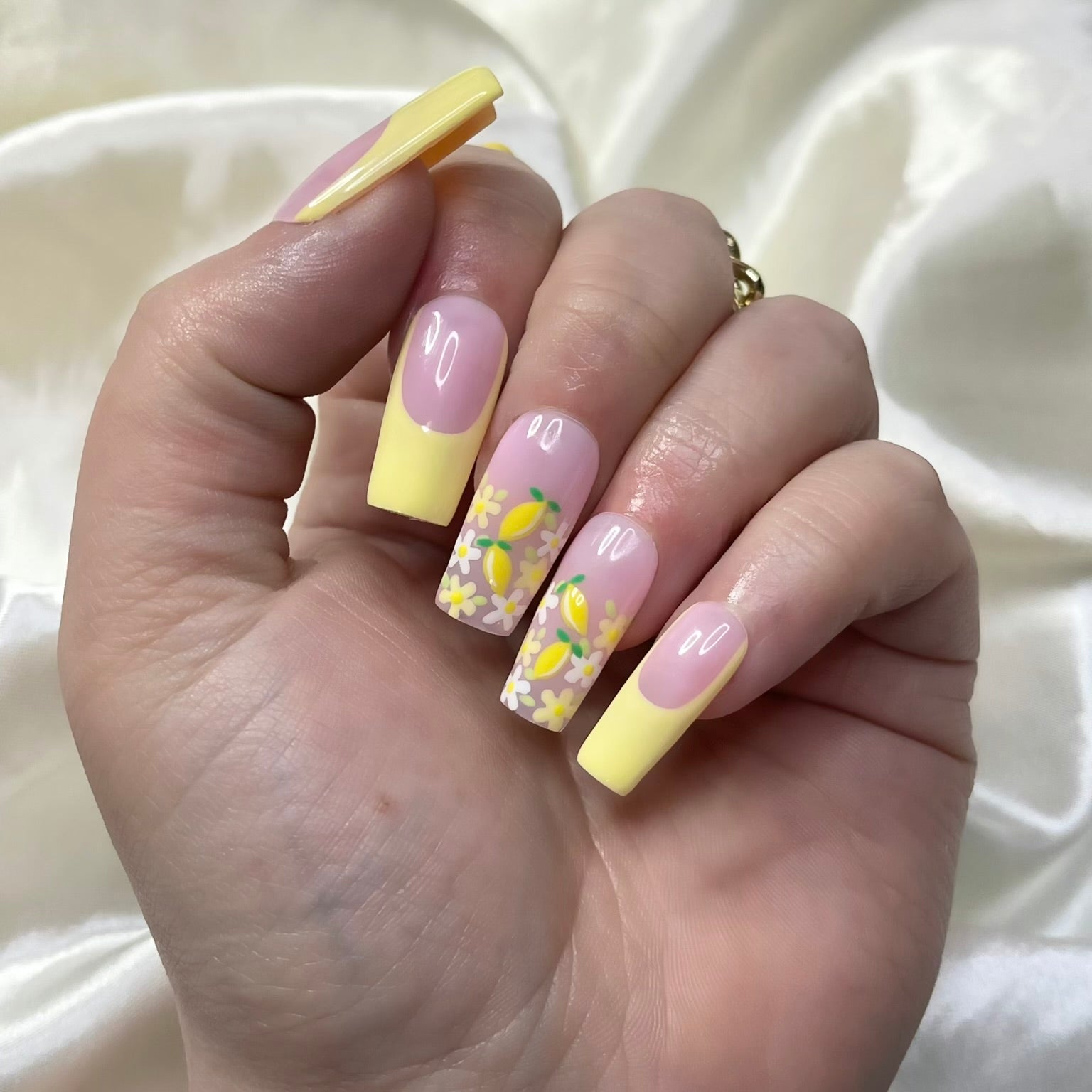 Lemon Meadow press-on nails feature vibrant yellow French tips, white and yellow flowers, golden centres, hand-painted lemons, and soft pinky nude bases for a fresh spring look.