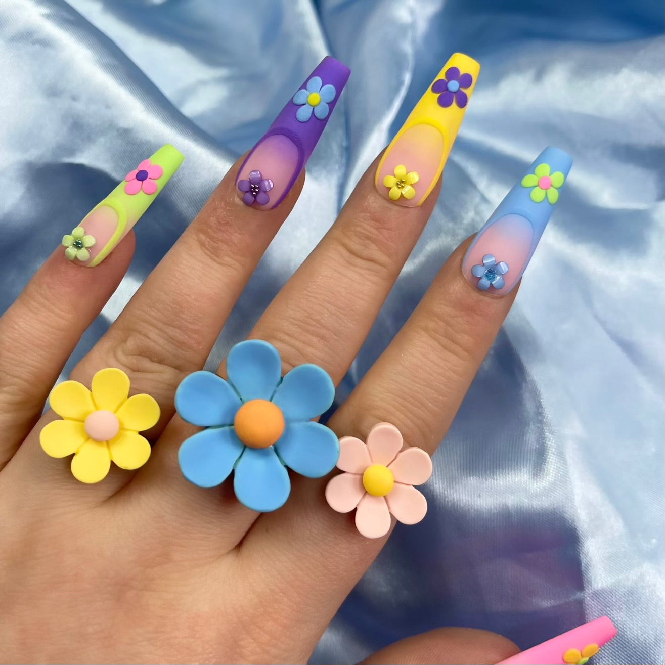 Spring Dream press-on nails feature a pastel ombre design in pink, blue, yellow, purple, and green with embossed French tips and 3D floral details for a chic spring look.