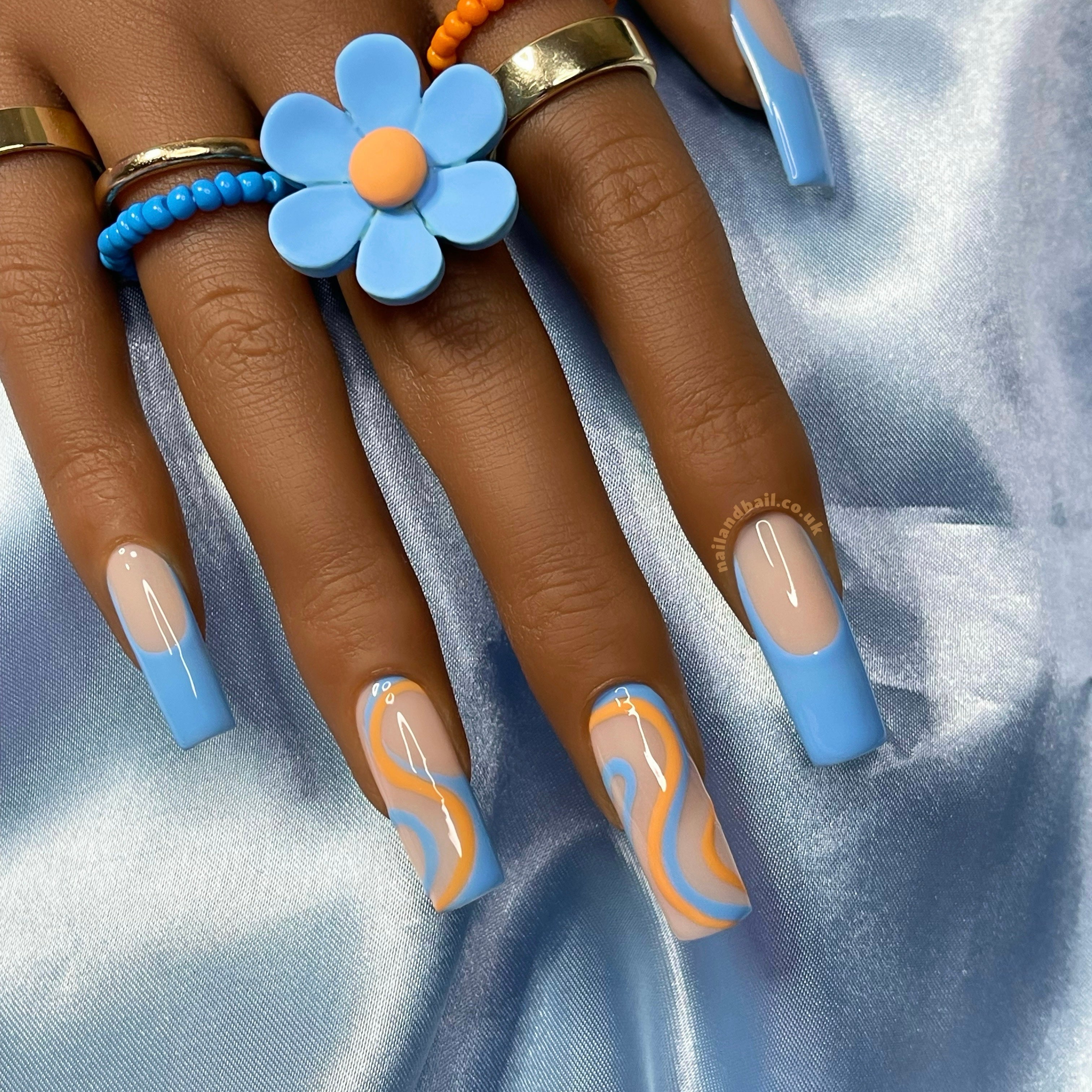 Summer press-on nails with blue French tips and orange swirl nail art