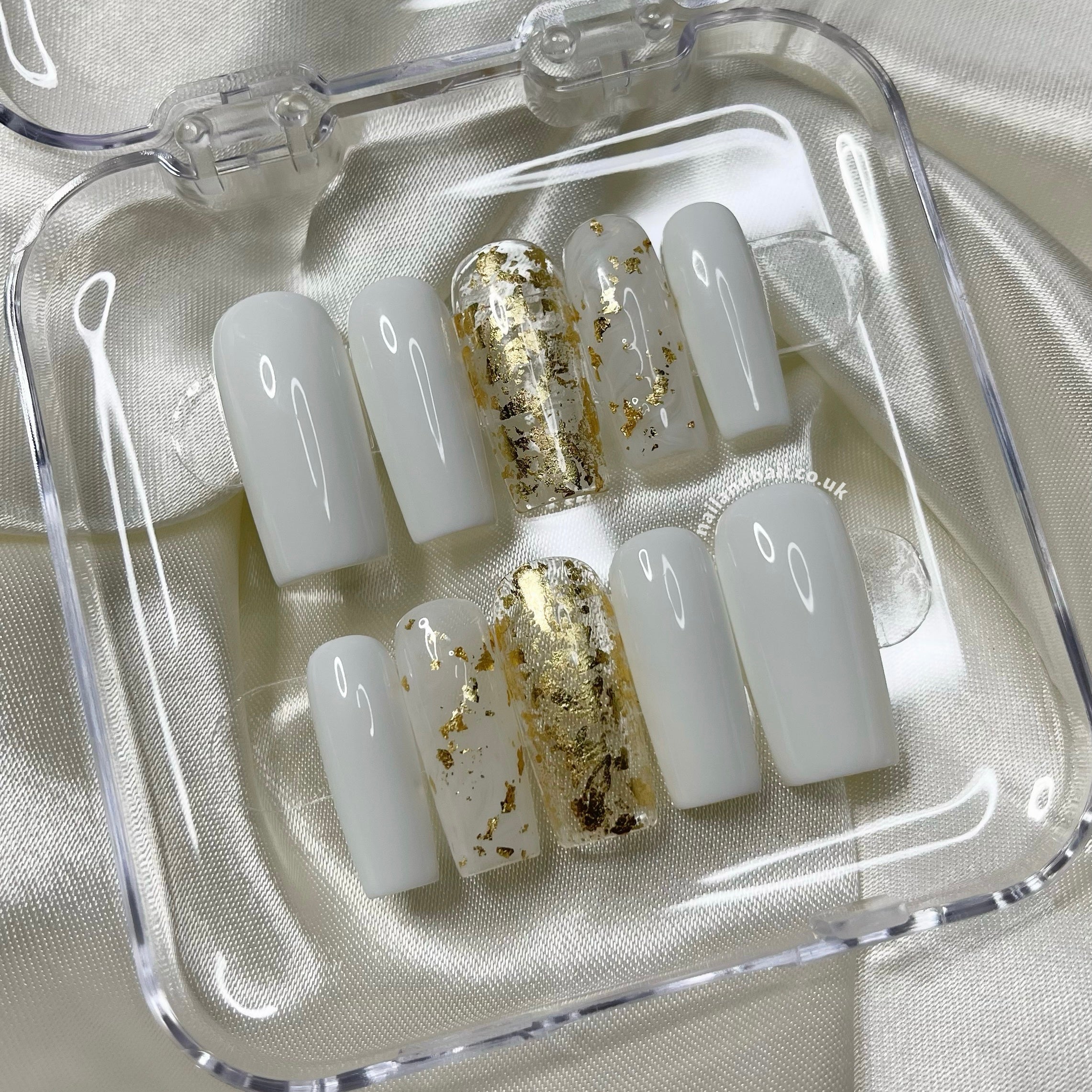 White press-on nails with gold foil accents, clear nails, and marble-inspired gold detailing