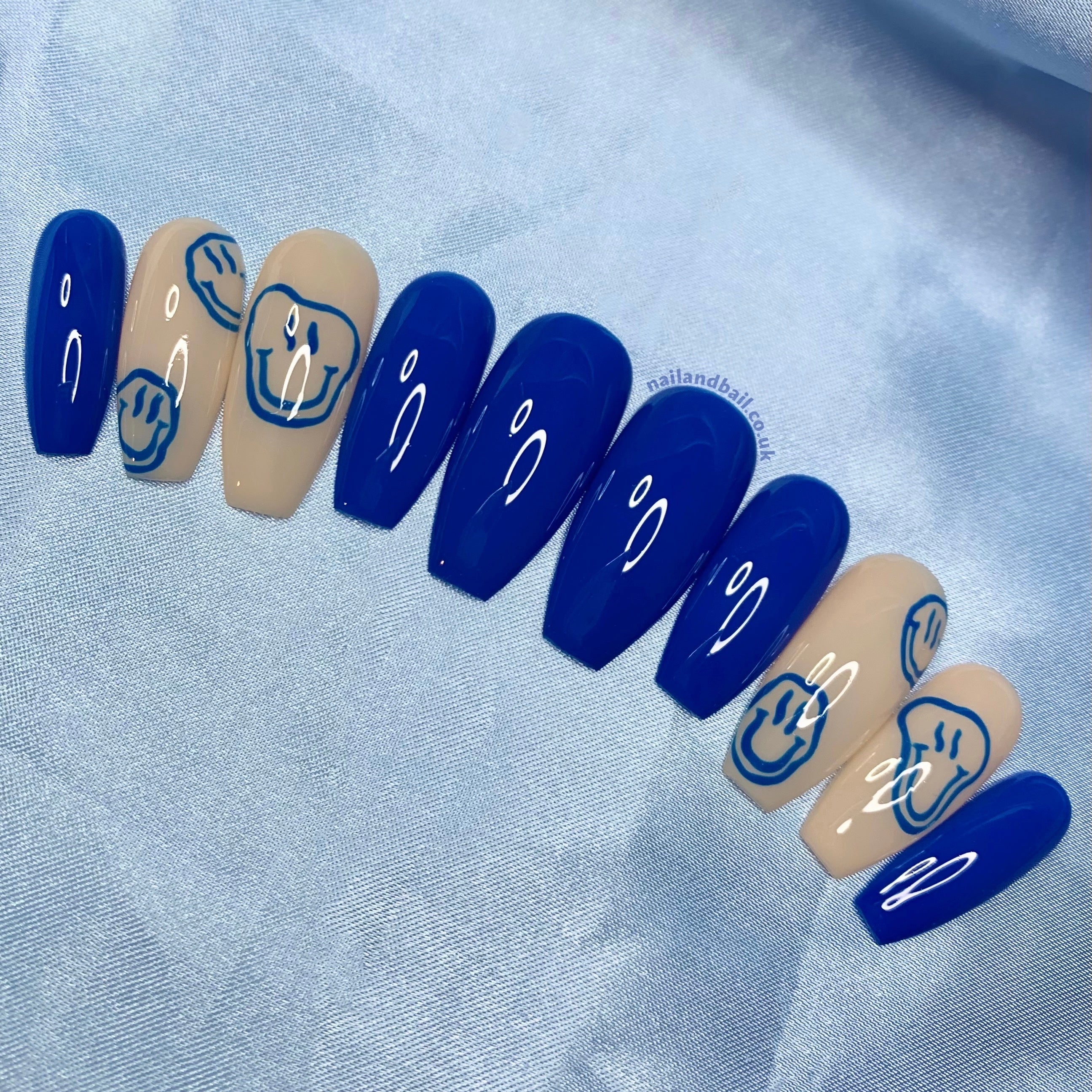 Dark blue press-on nails with hand-painted trippy smiley face nail art on nude accent nails