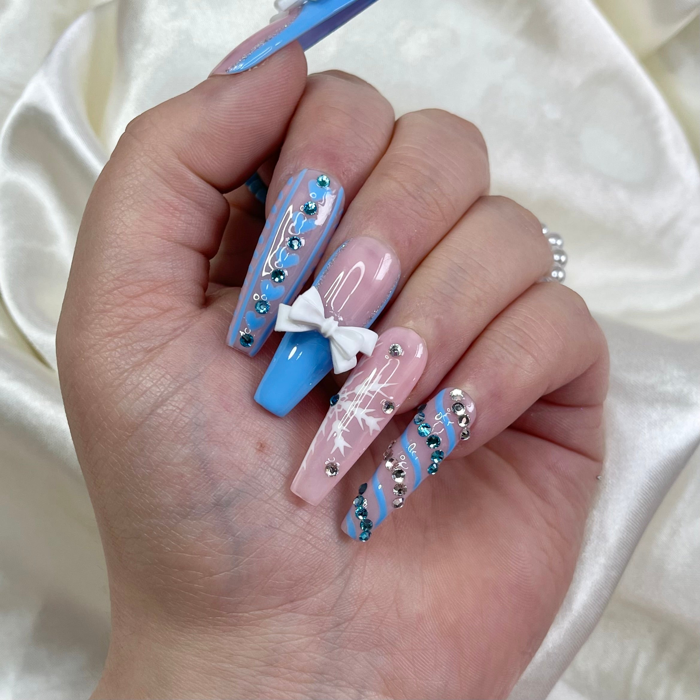 Winter press-on nails with blue French tips, white bows, snowflake nail art, and crystal details
