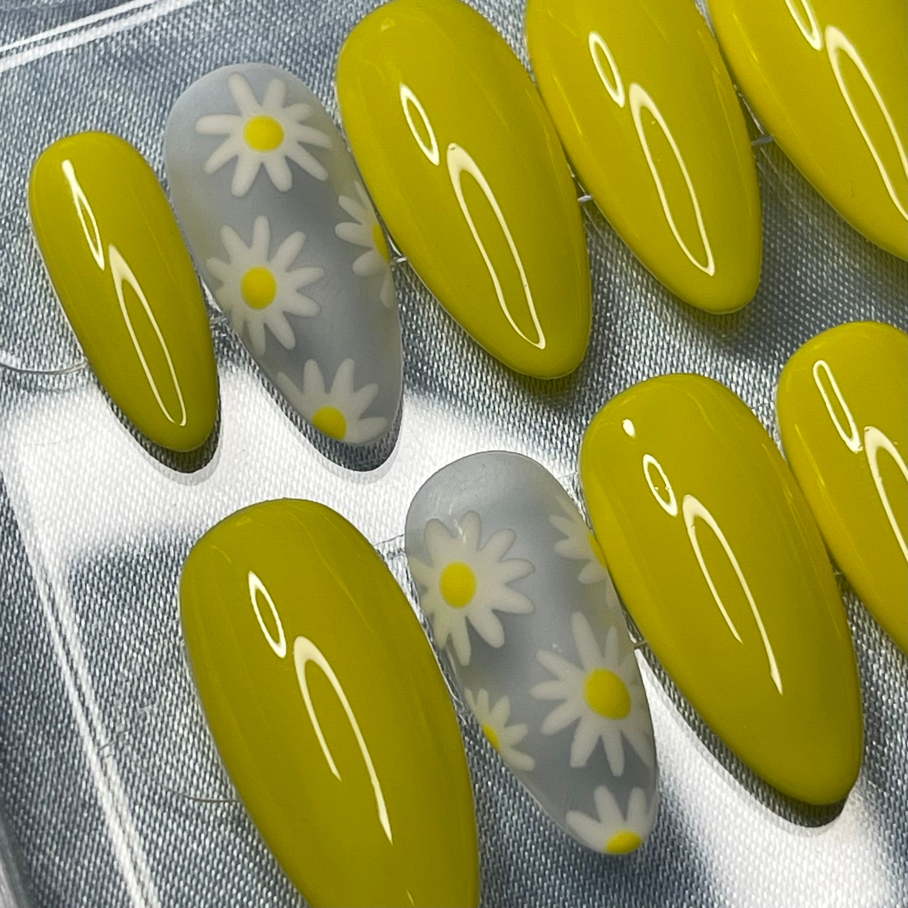 Glossy yellow press-on nails with delicate hand-painted white daisy nail art