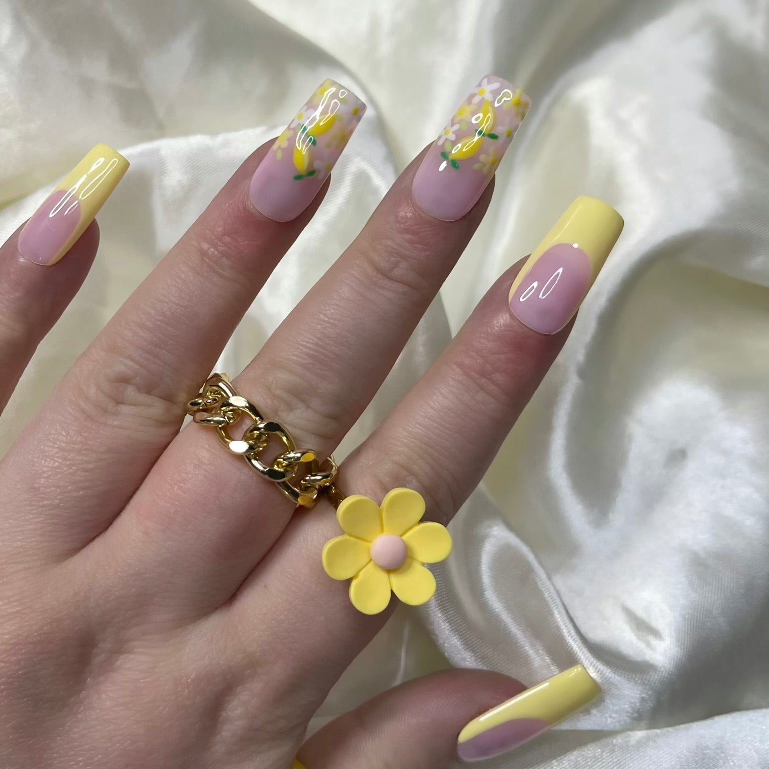 Lemon Meadow press-on nails feature vibrant yellow French tips, white and yellow flowers, golden centres, hand-painted lemons, and soft pinky nude bases for a fresh spring look.