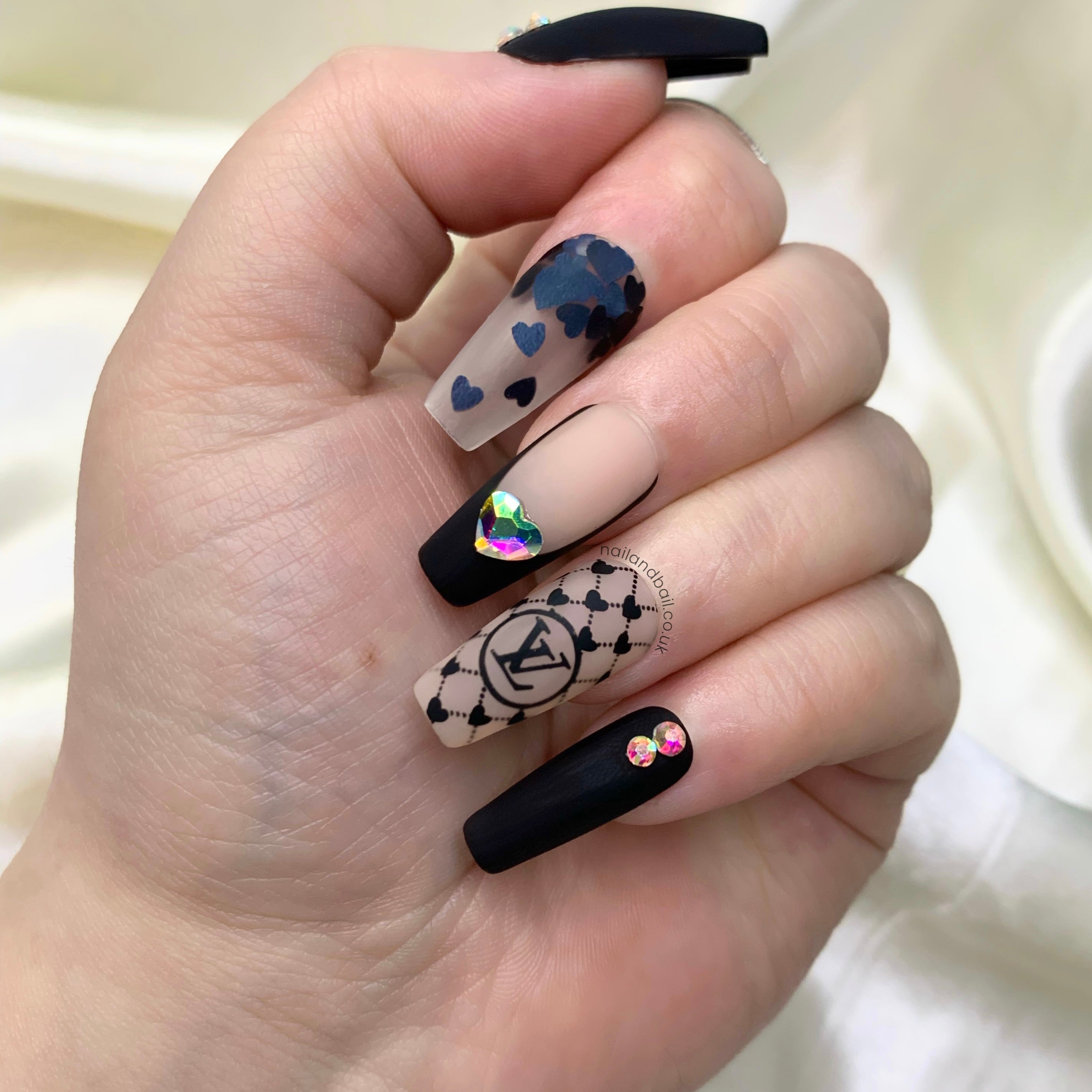Matte black press-on nails with black heart nail art, French tips, crystals, and luxury-inspired details