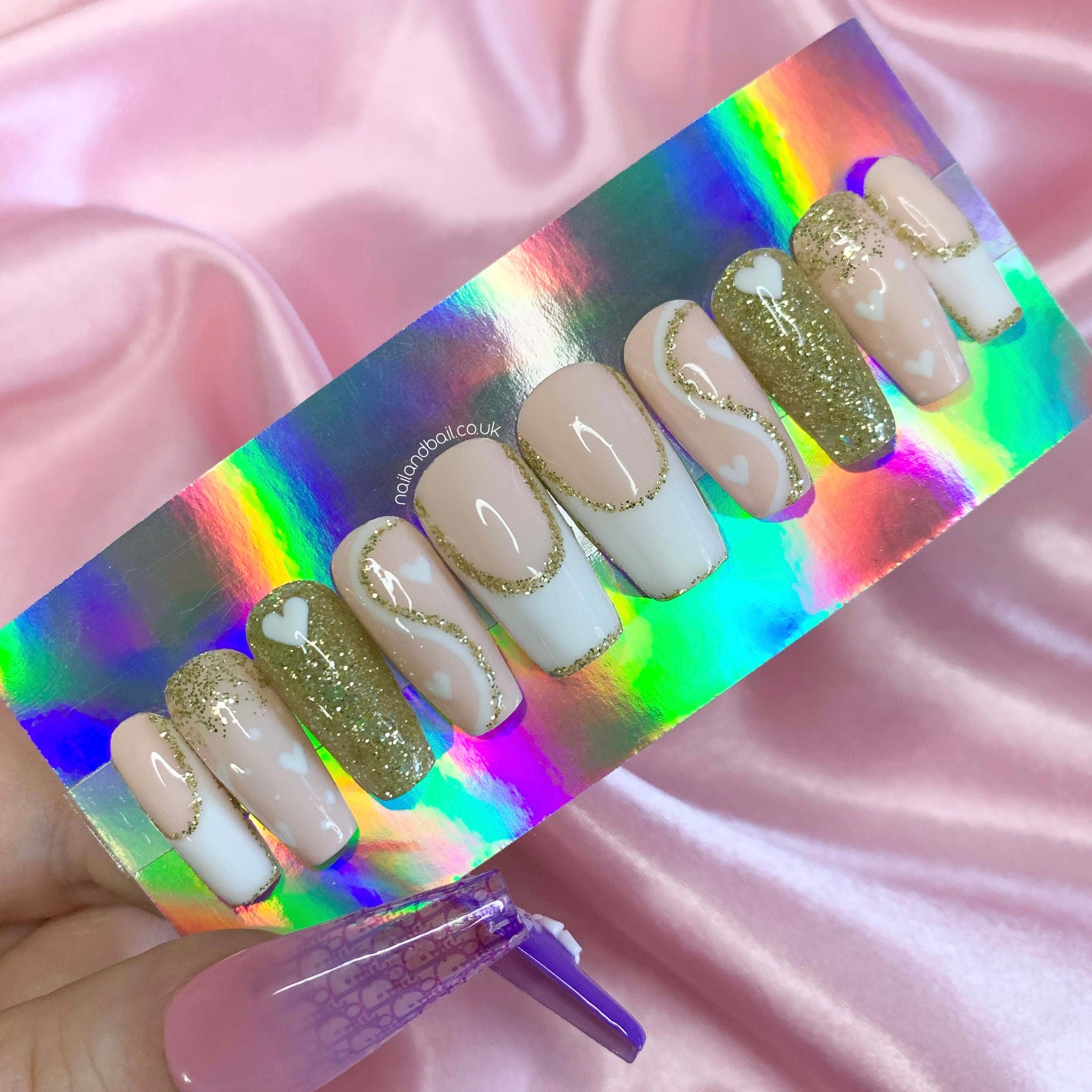 Nude and white French tip press-on nails with gold glitter, heart nail art, and elegant glam details