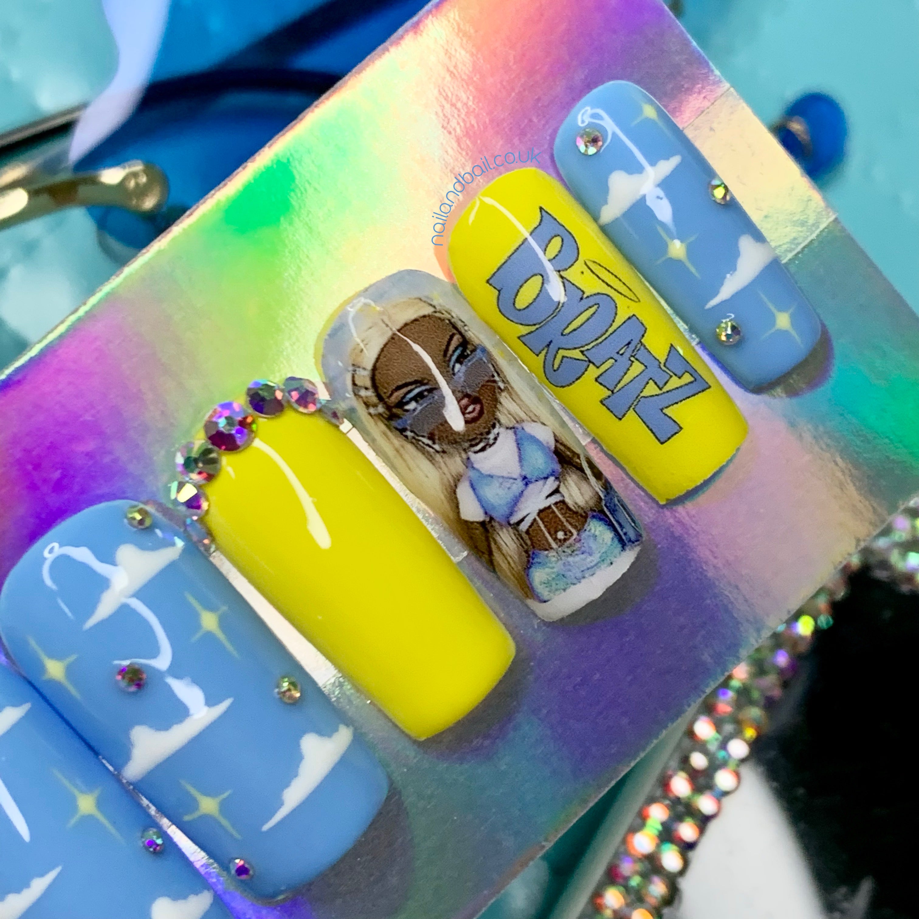 Blue press-on nails with white cloud nail art, stars, and crystal details