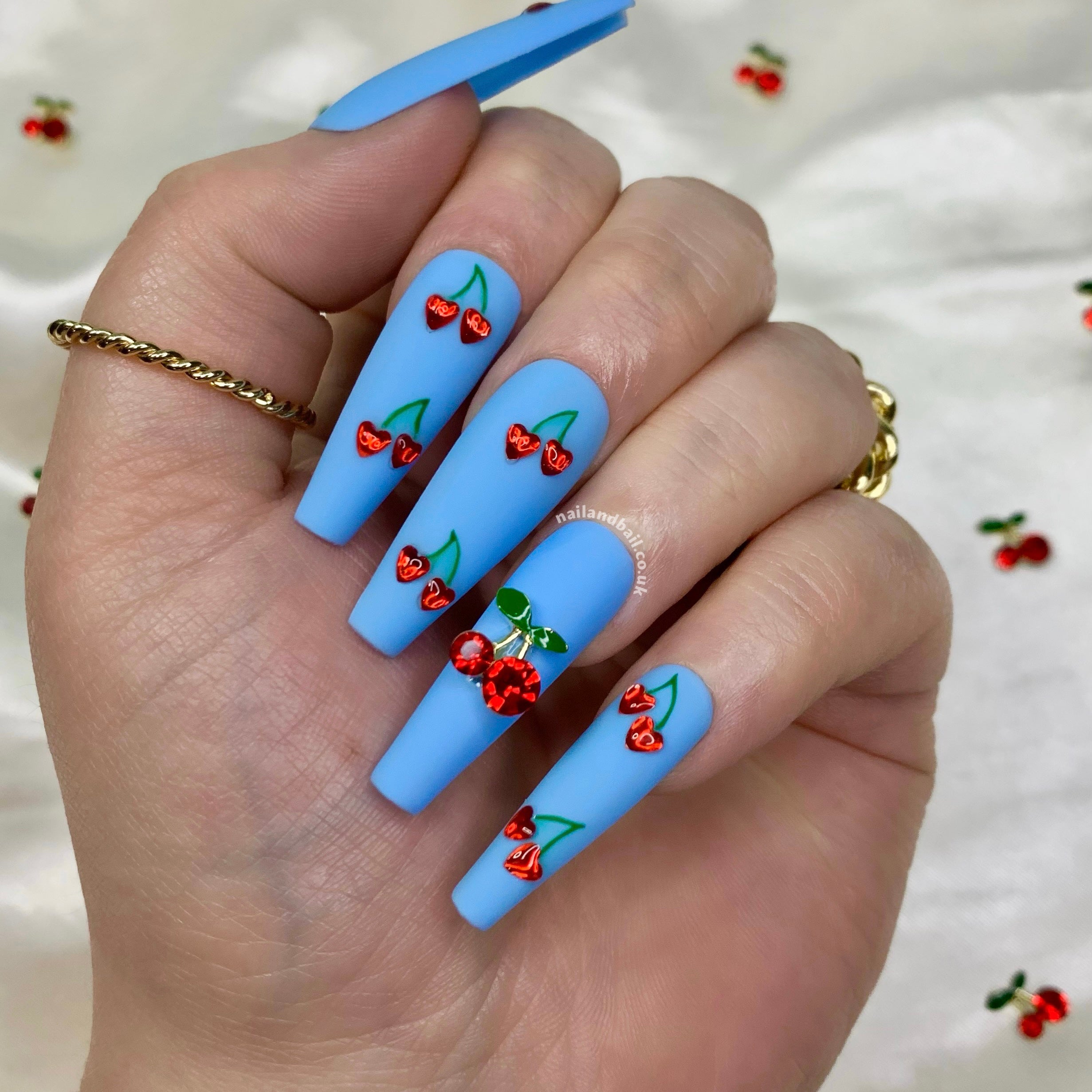 Hand-painted glossy cherry nail art on matte blue press-on nails