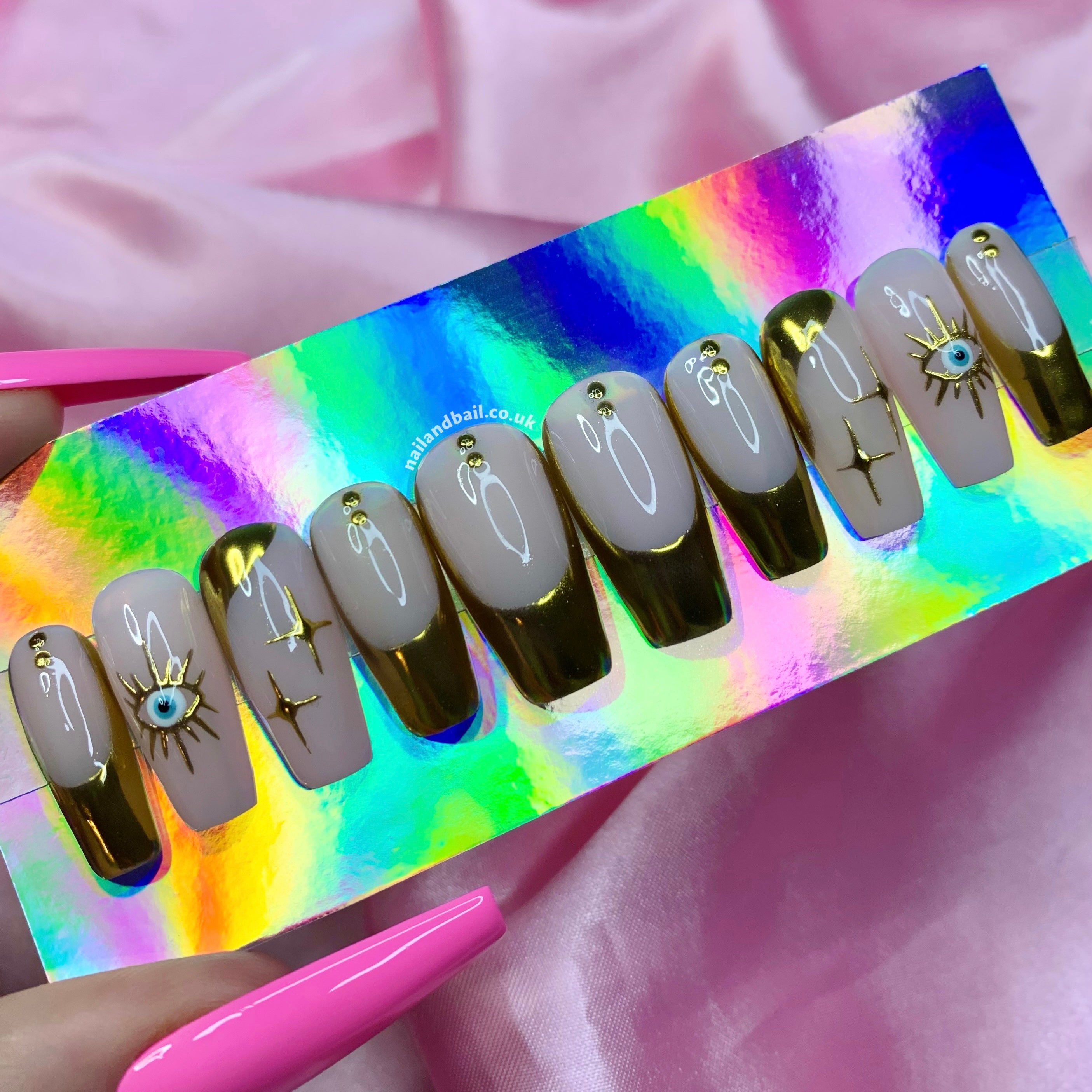 Nude press-on nails with gold French tips, evil eye nail art, and gold star details