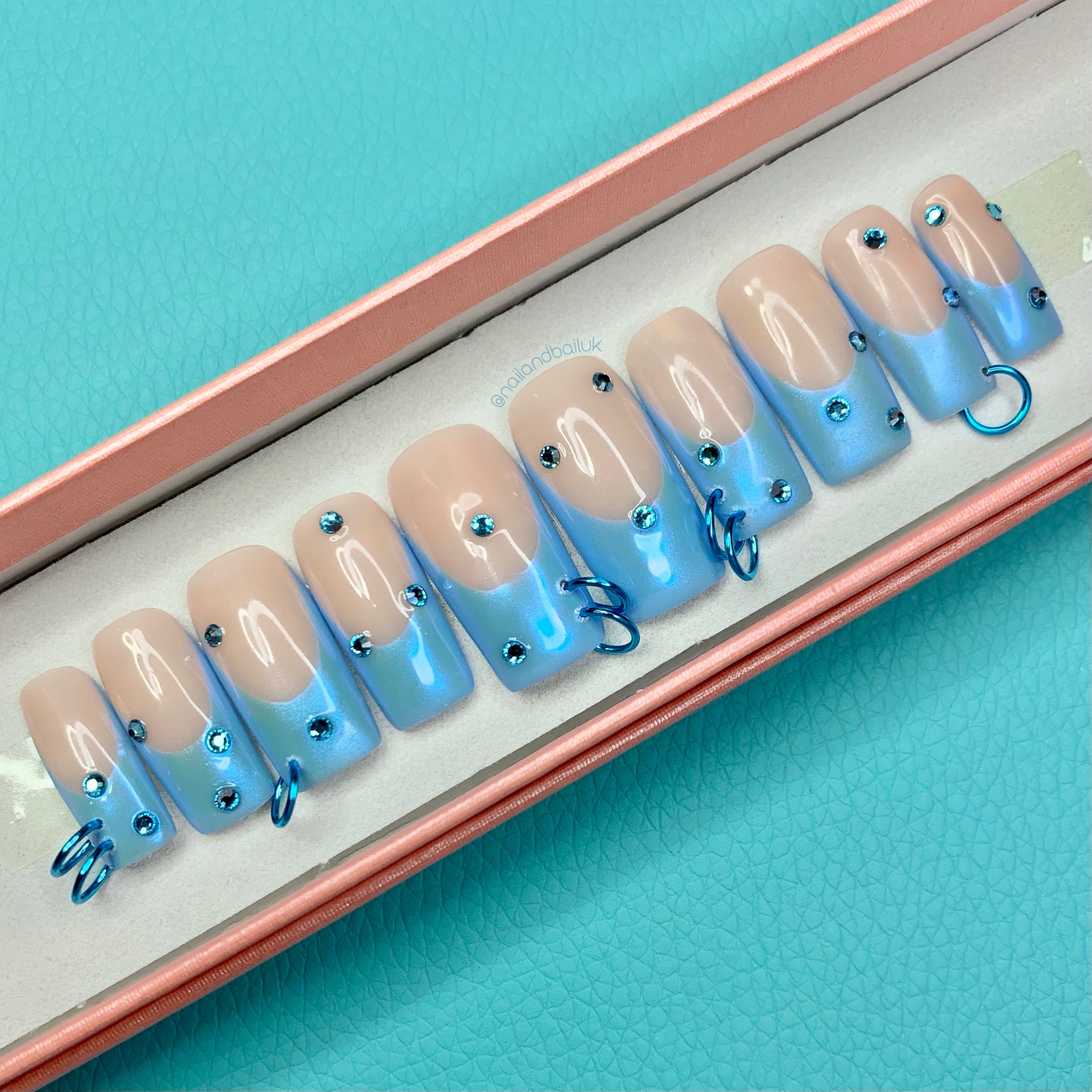 Nude press-on nails with blue chrome French tips, blue crystals, and statement chain link details