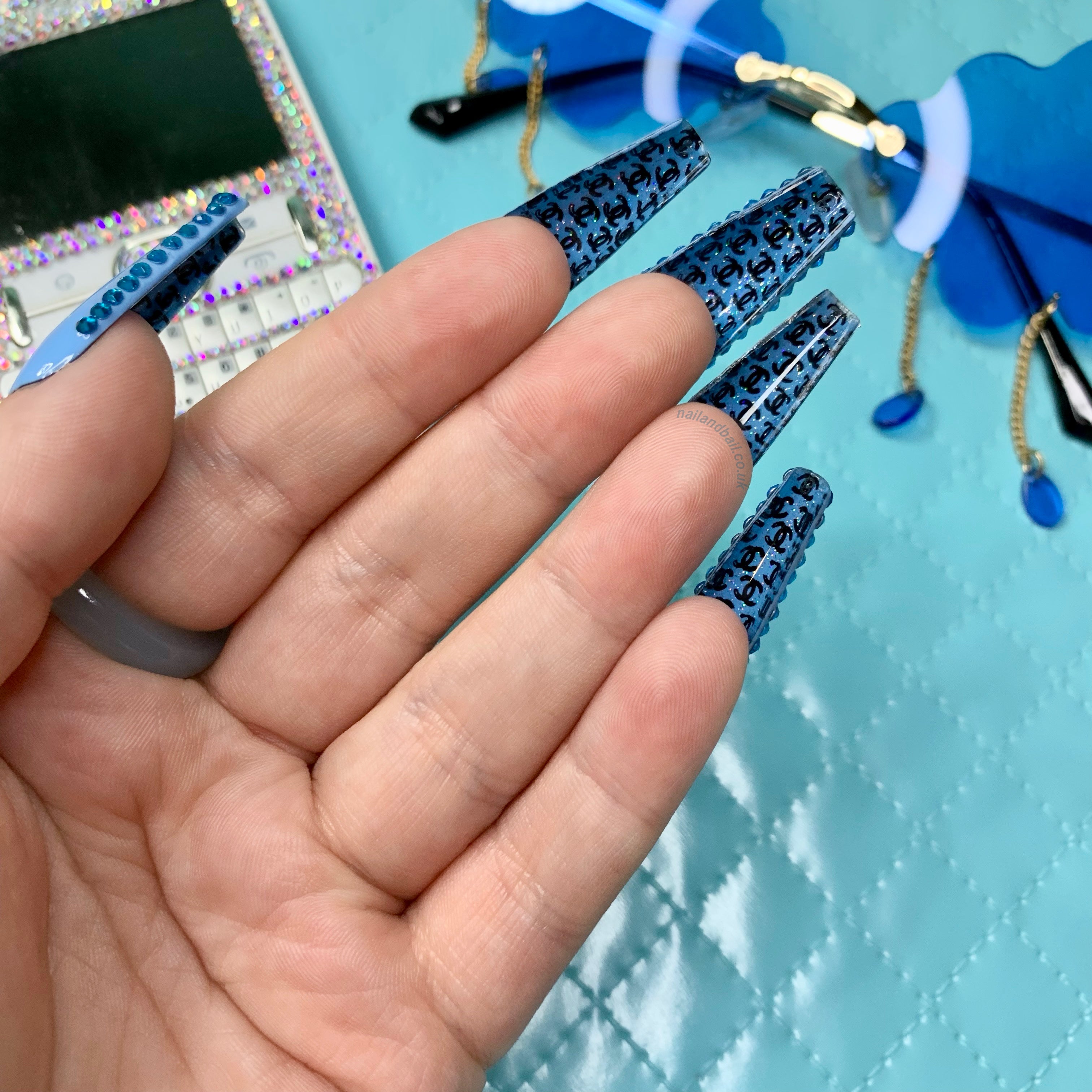 Luxury-inspired blue press-on nails with hidden artwork beneath the nails and crystal details