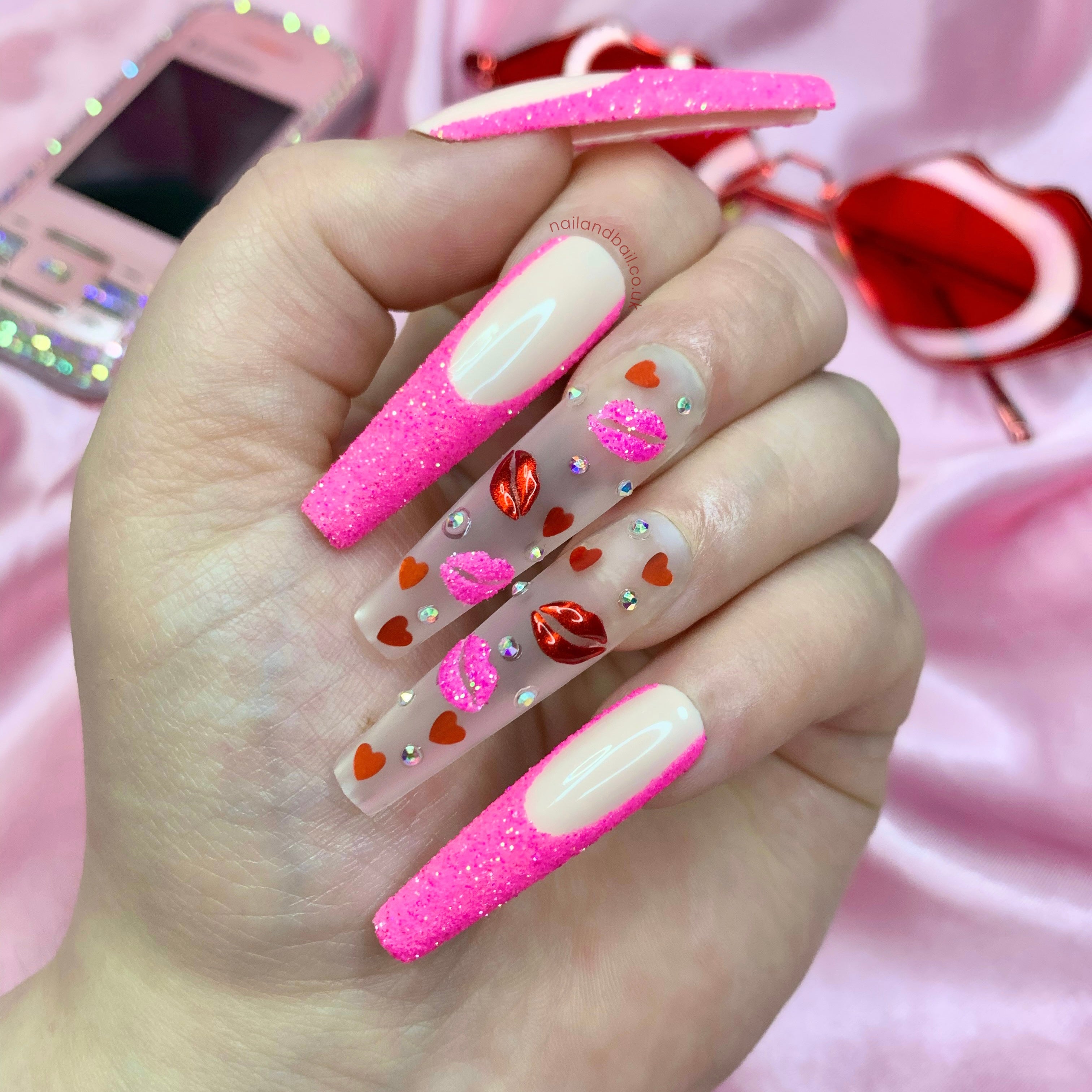 Nude press-on nails with pink glitter French tips, heart sequins, chrome lip nail art, and crystals
