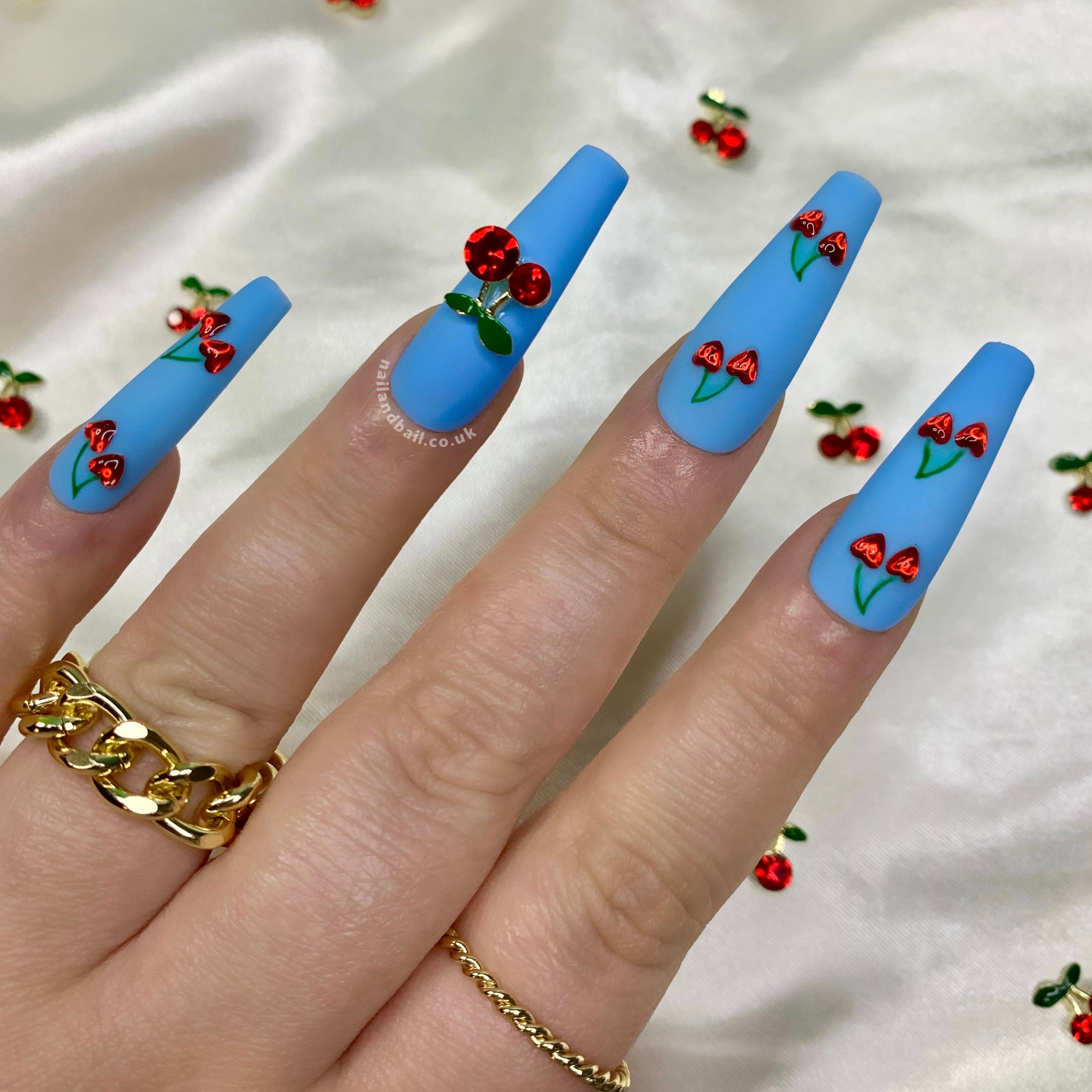Matte blue press-on nails with fruity cherry-inspired nail art