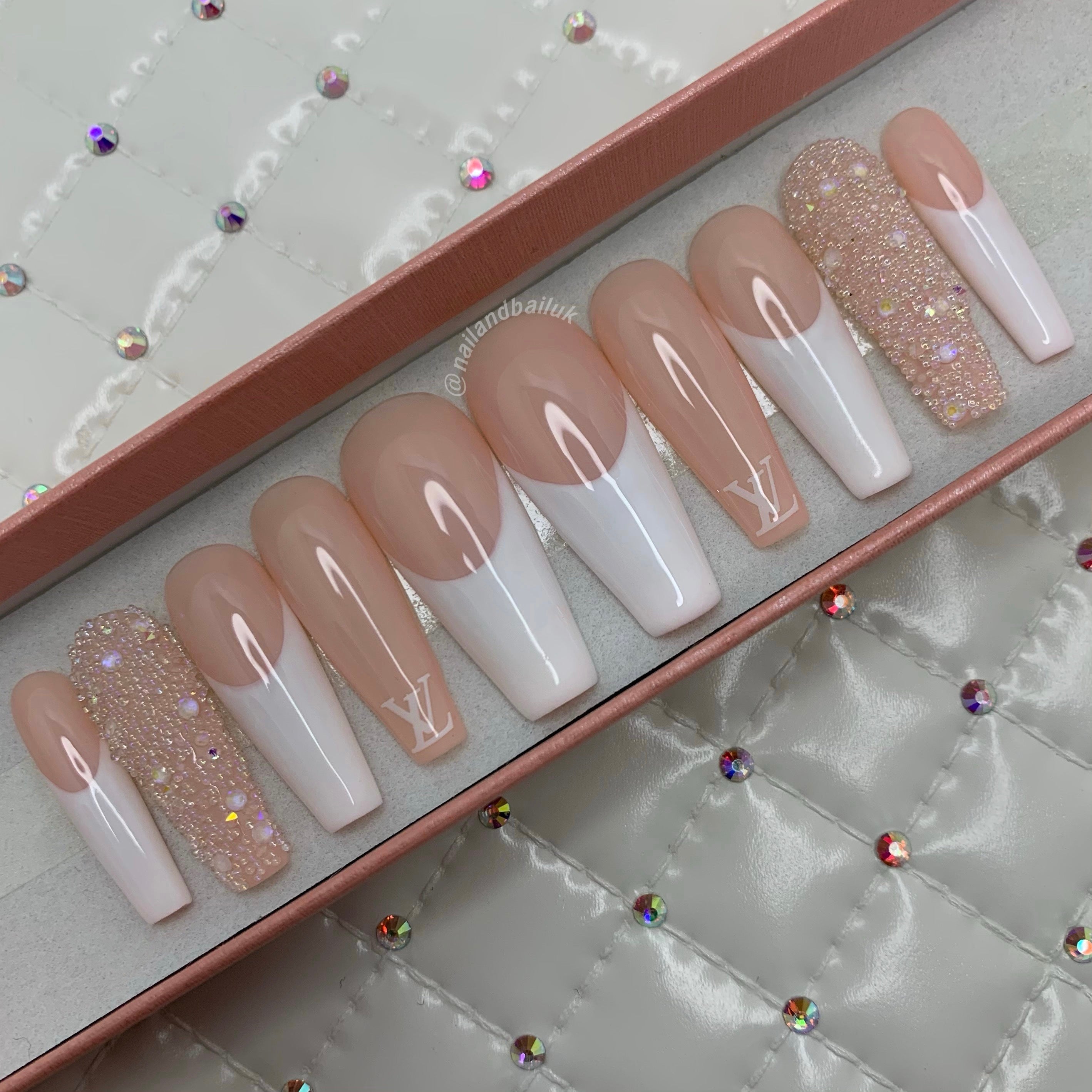Nude press-on nails with white French tips, luxury-inspired prints, crystals, and pearl bead detailing