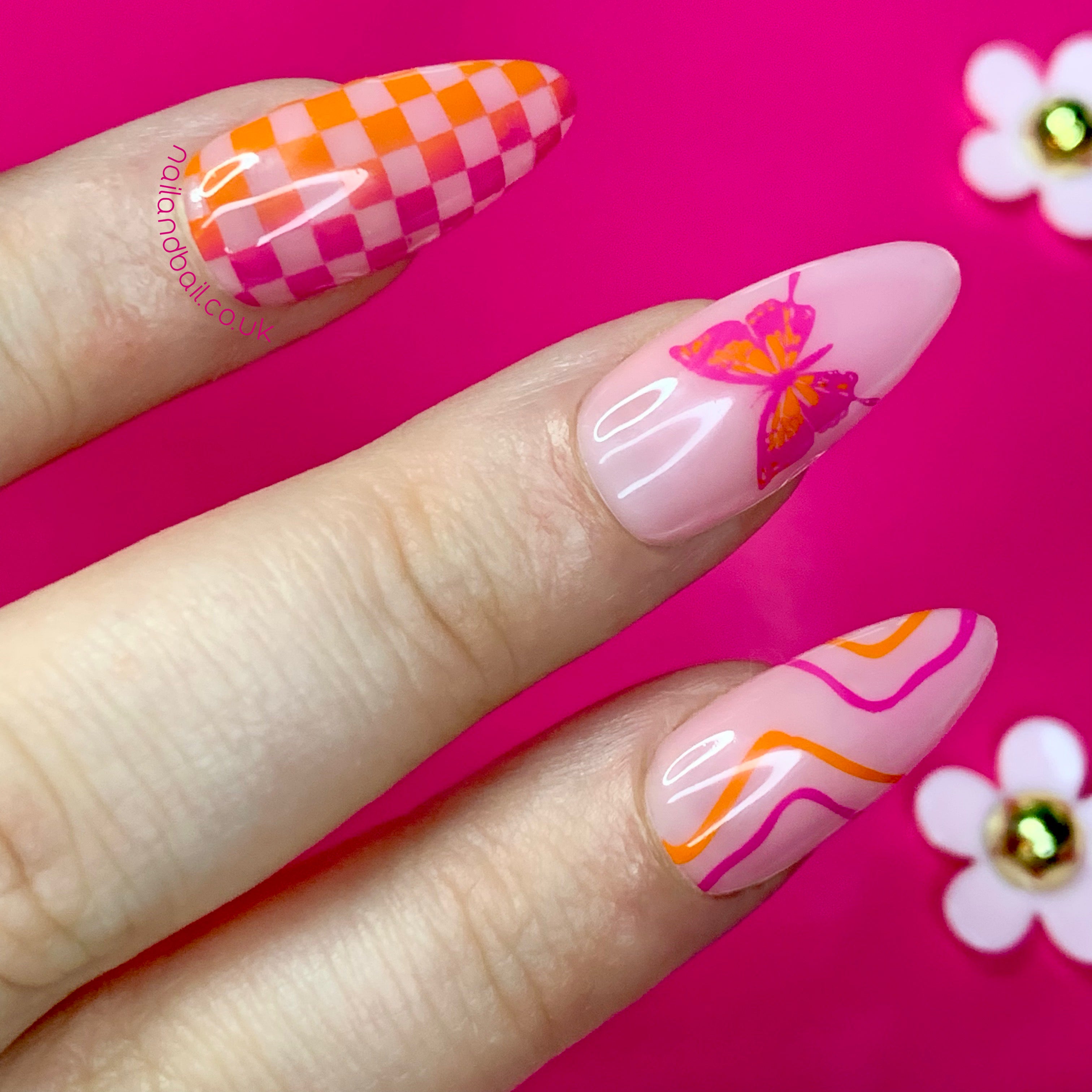 Colourful orange and pink press-on nails with butterfly nail art, checkered patterns, and squiggle details