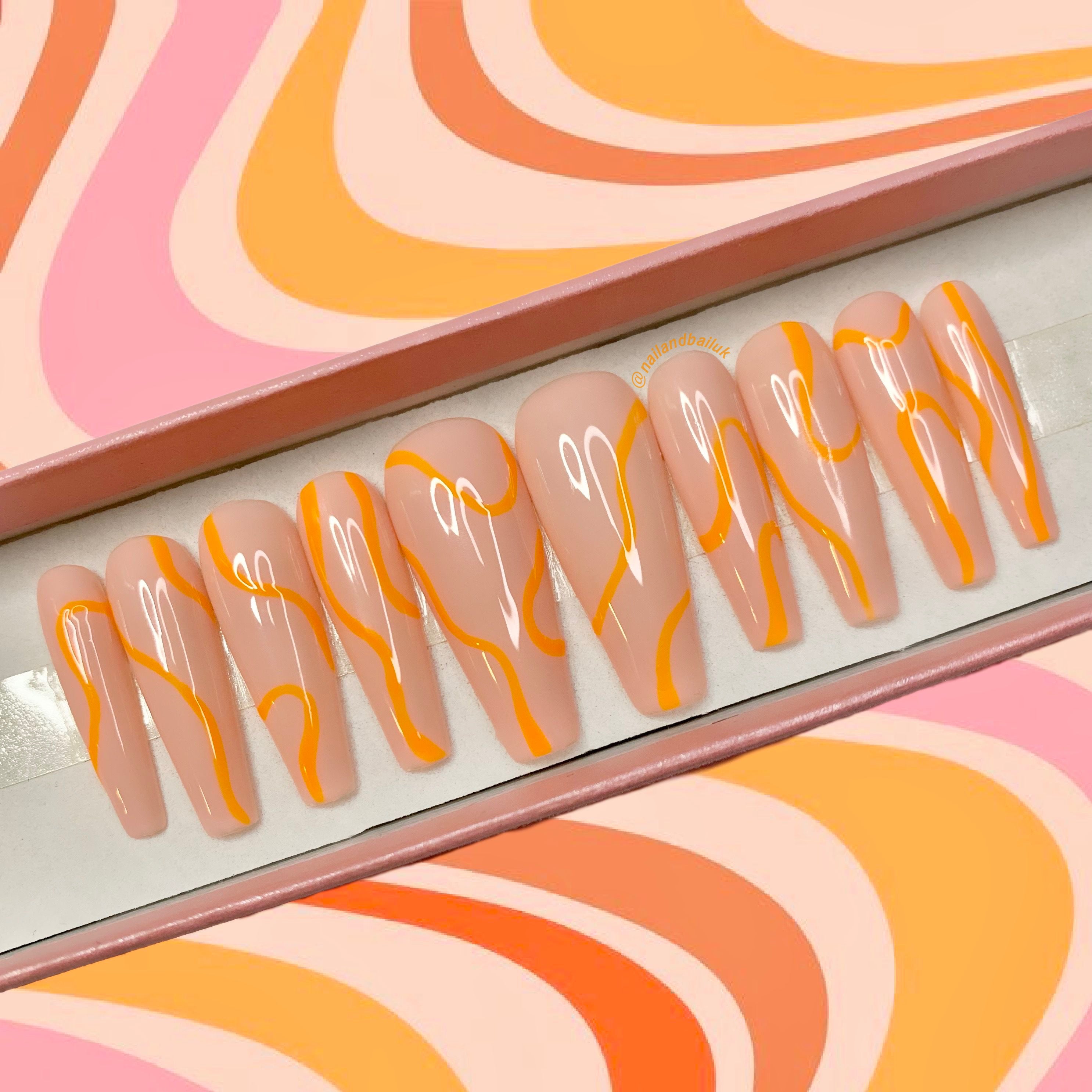 Glossy nude press-on nails with vibrant orange abstract swirl nail art