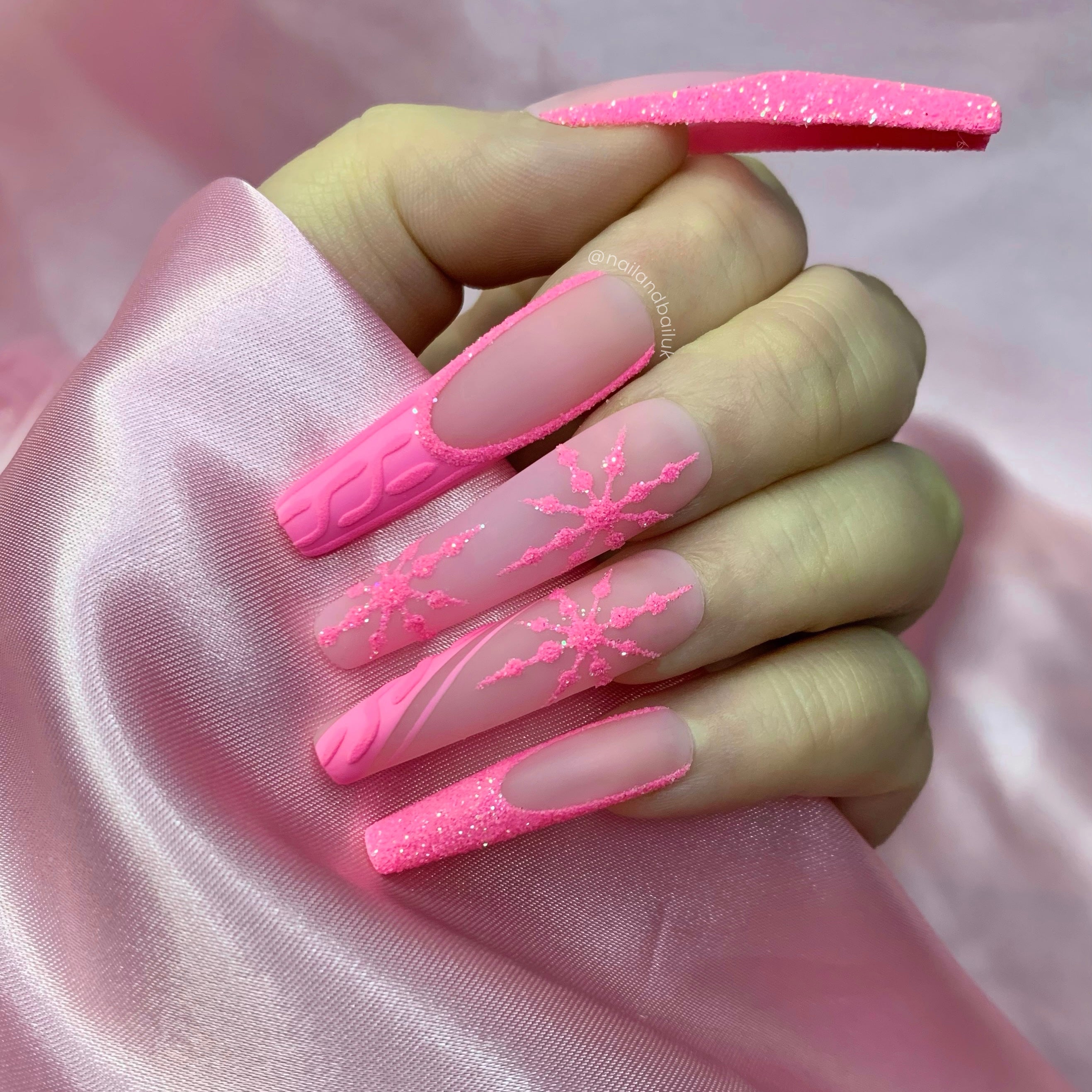Pink winter press-on nails with sugared glitter French tips, snowflake nail art, and embossed sweater details