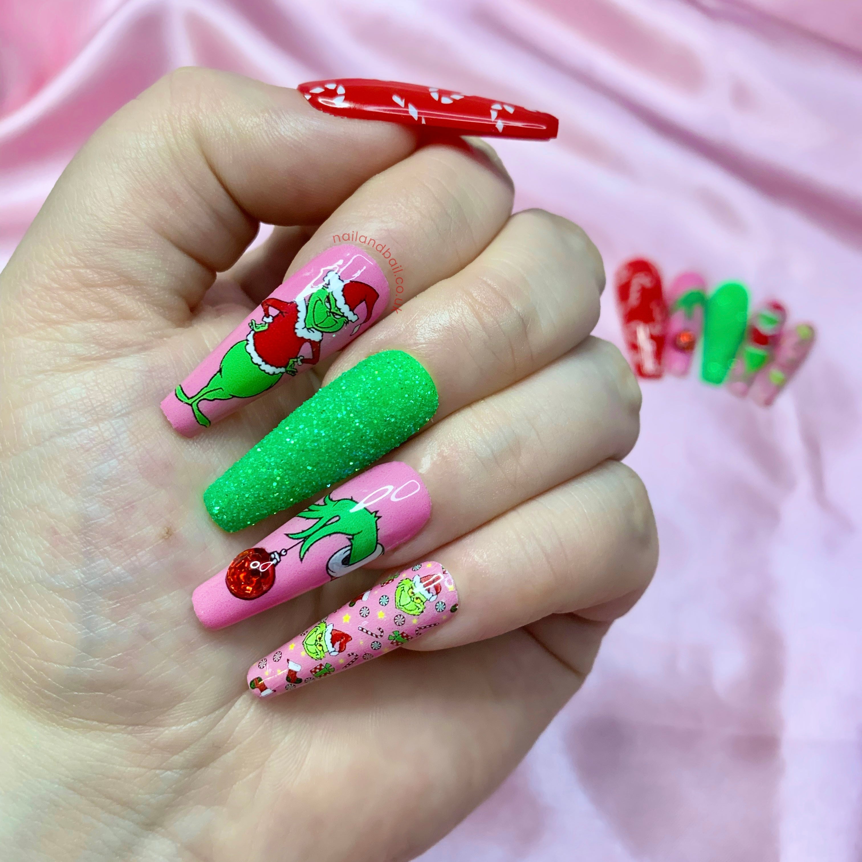 Pink Grinch press-on nails with festive nail art, sugared glitter textures, and raised bauble details