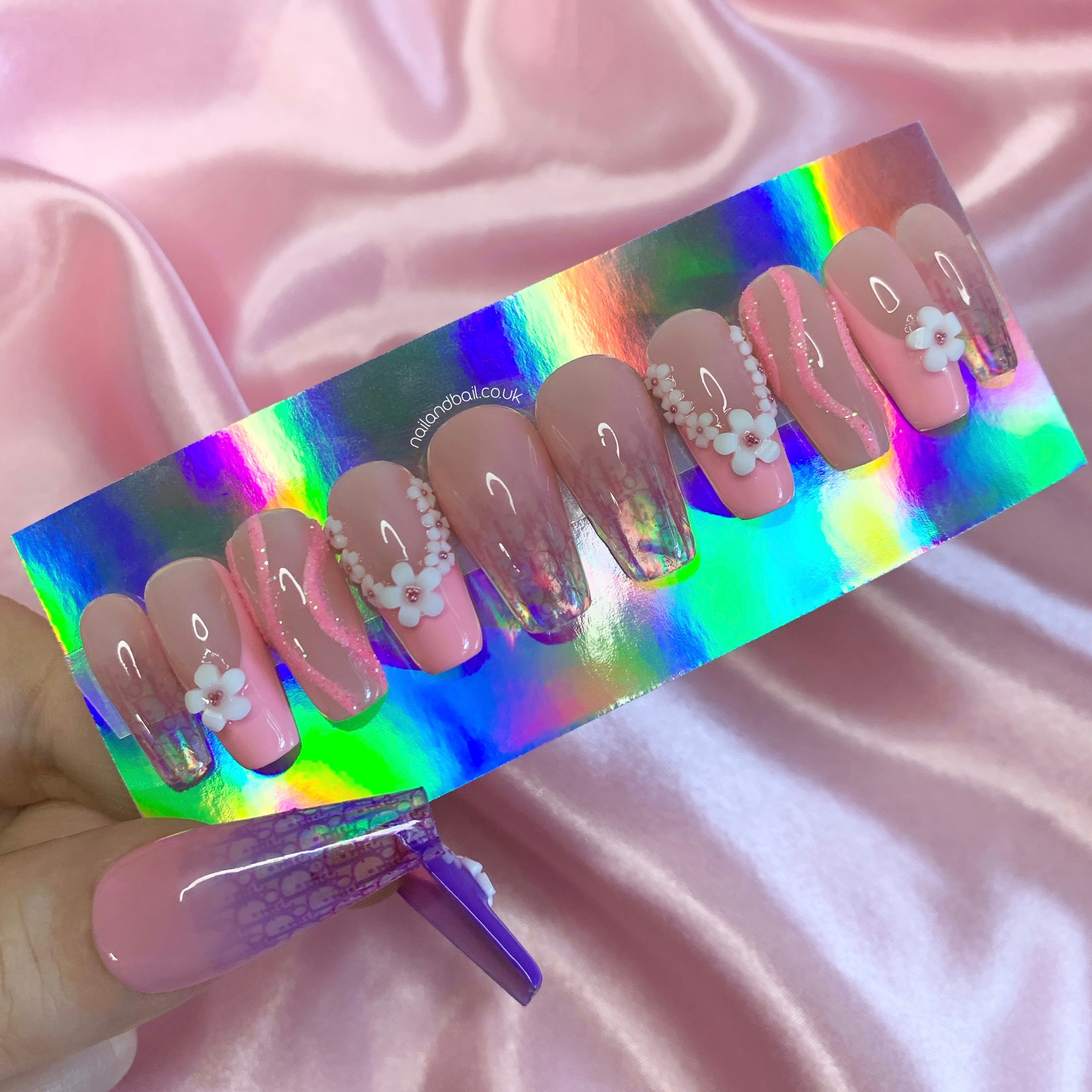Nude ombré press-on nails with pink floral charms, glitter swirls, and luxury-inspired nail art