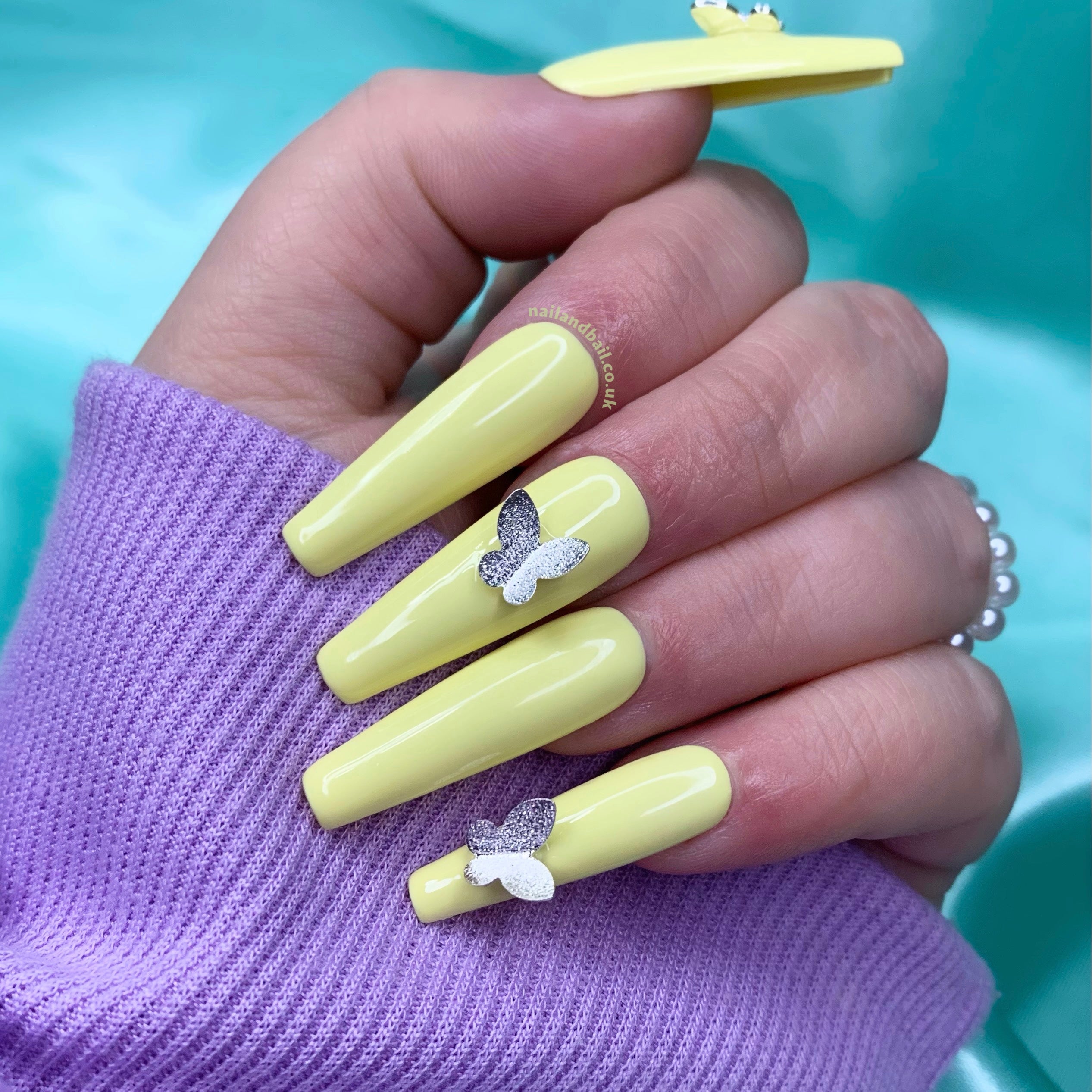 Pastel yellow press-on nails with silver butterfly charms and whimsical nail art