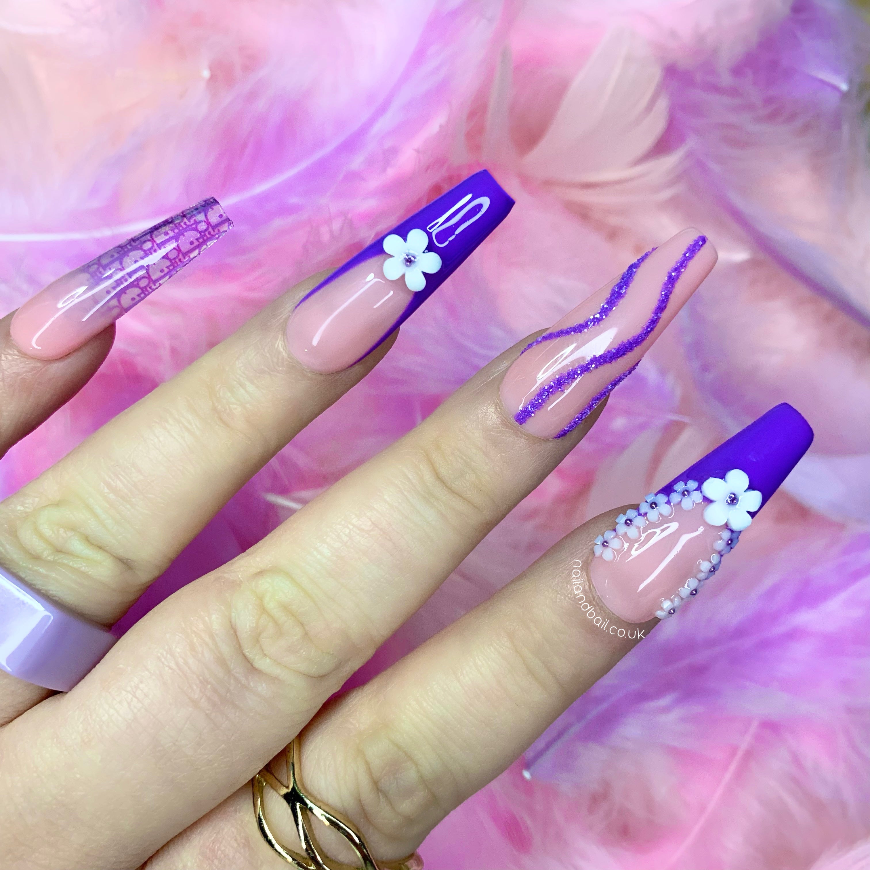 Nude ombré press-on nails with dark purple floral charms, glitter swirls, and luxury-inspired nail art