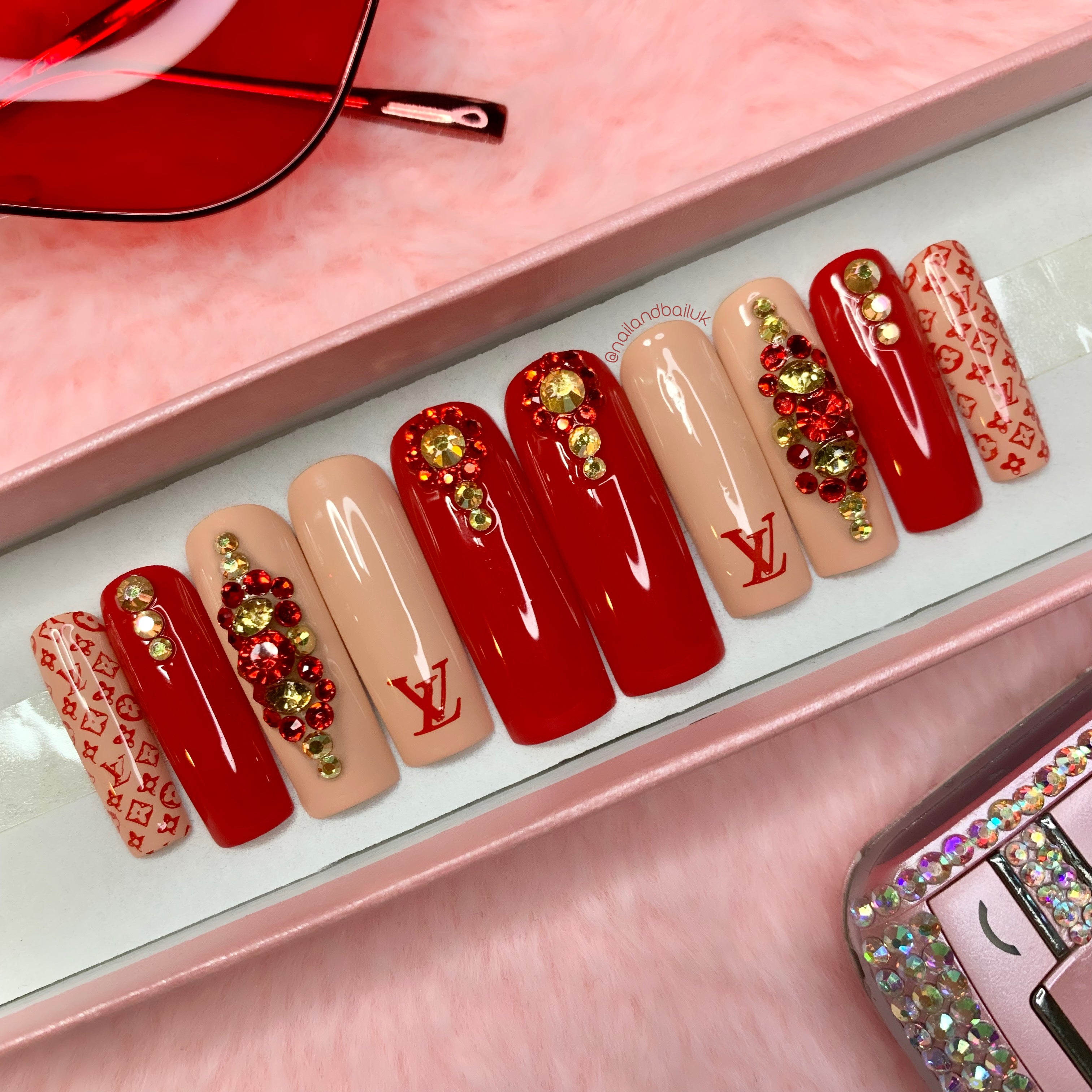 Red and nude press-on nails with sparkling gold and red crystal embellishments