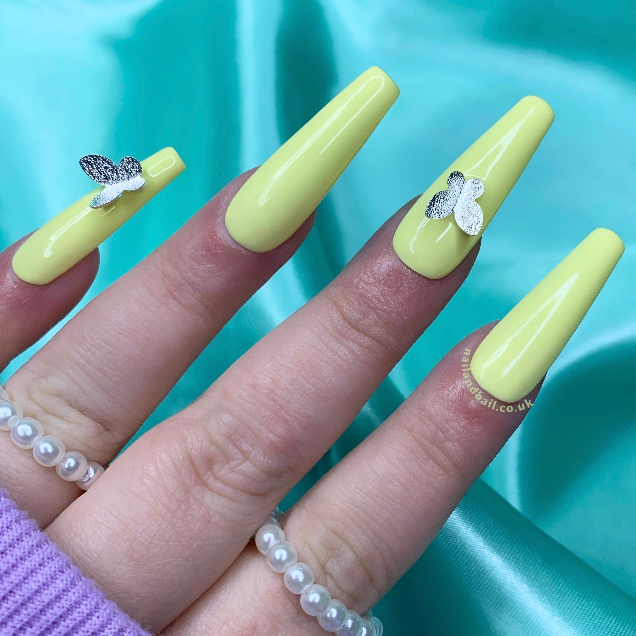 Silver butterfly charm nail art on pastel yellow press-on nails