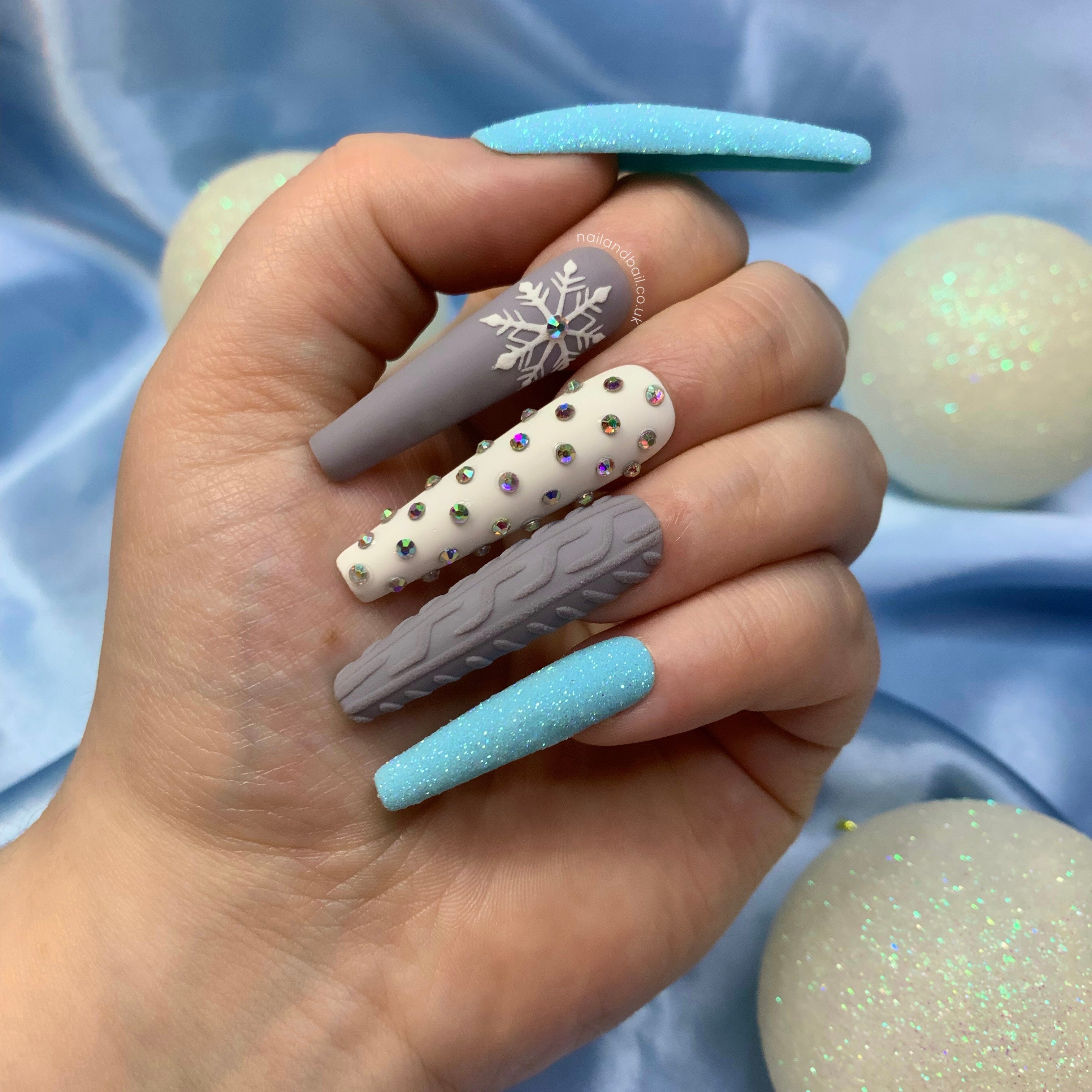 Winter press-on nails with blue sugared glitter, embossed snowflake nail art, sweater patterns, and silver crystals