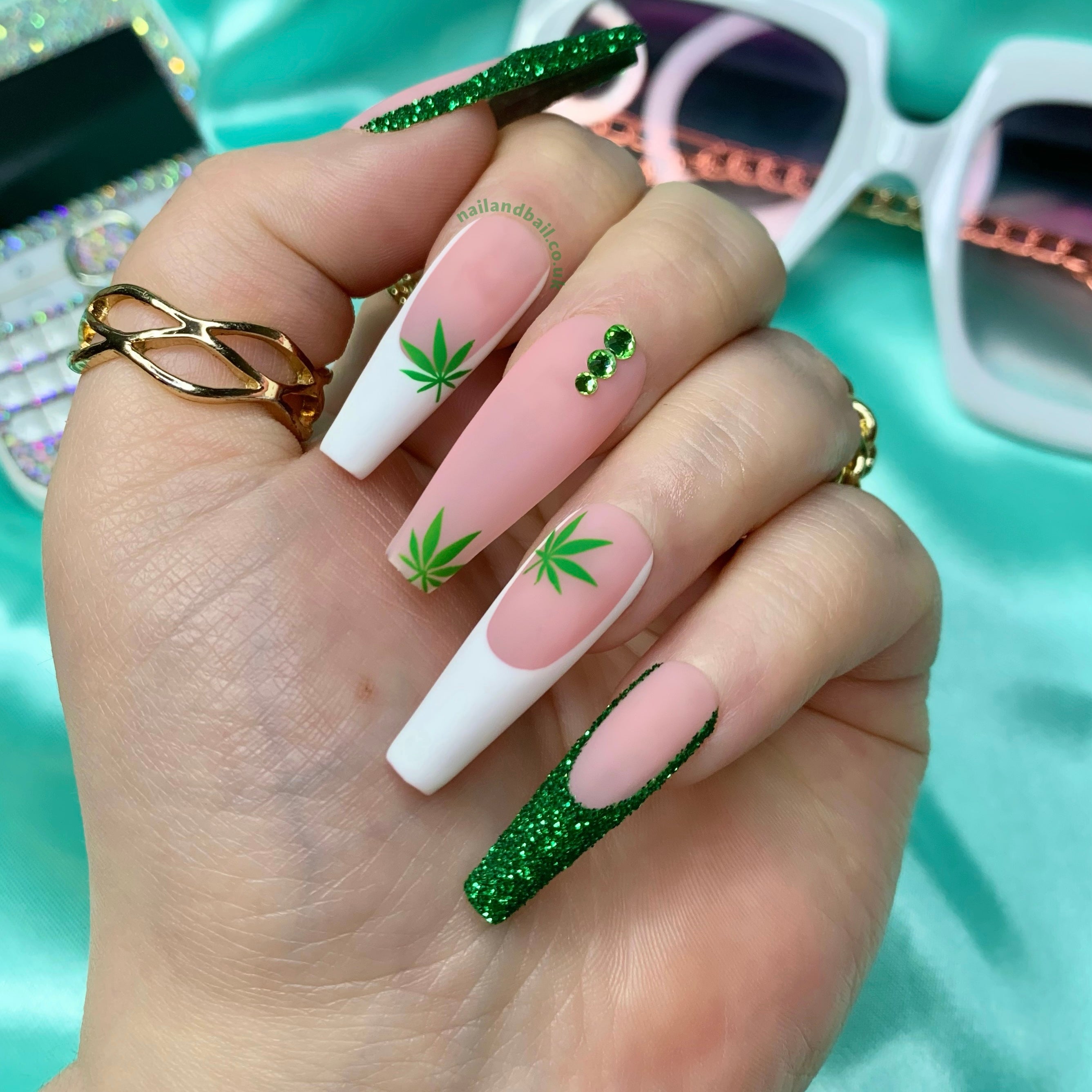 Nude and white French tip press-on nails with glitter details, green leaf nail art, and crystals