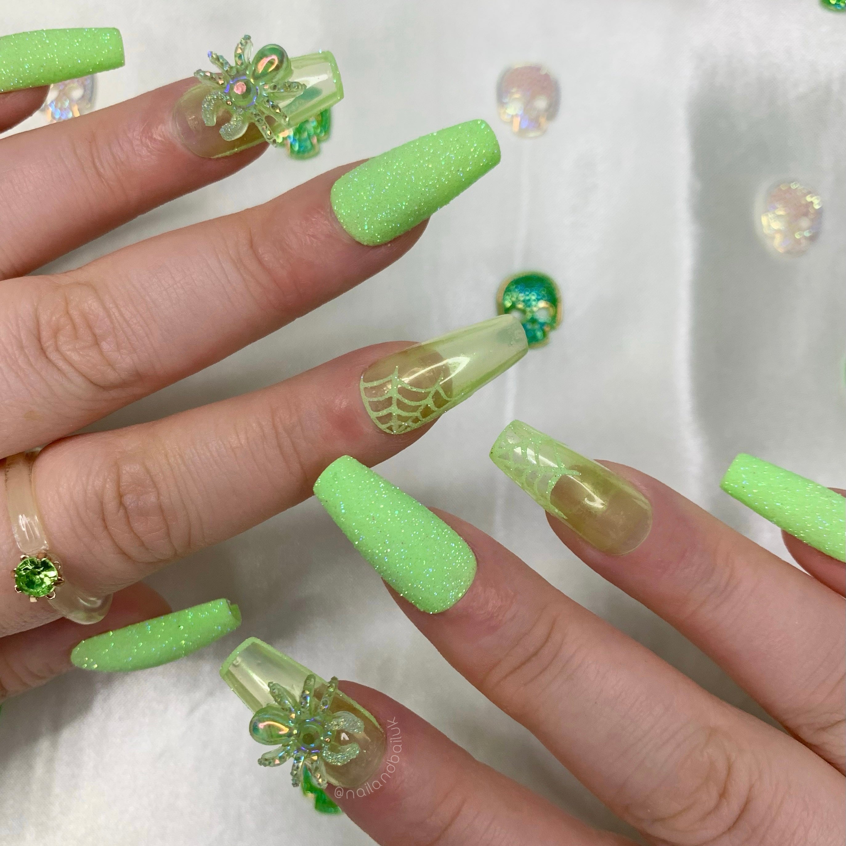 Green glitter Halloween press-on nails with iridescent chrome finishes, spiderweb nail art, and crystal charms