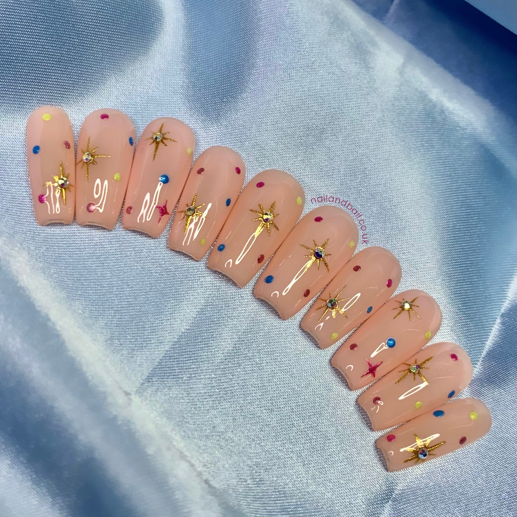Nude press-on nails with gold chrome stars, colourful chrome dots, and crystal nail art